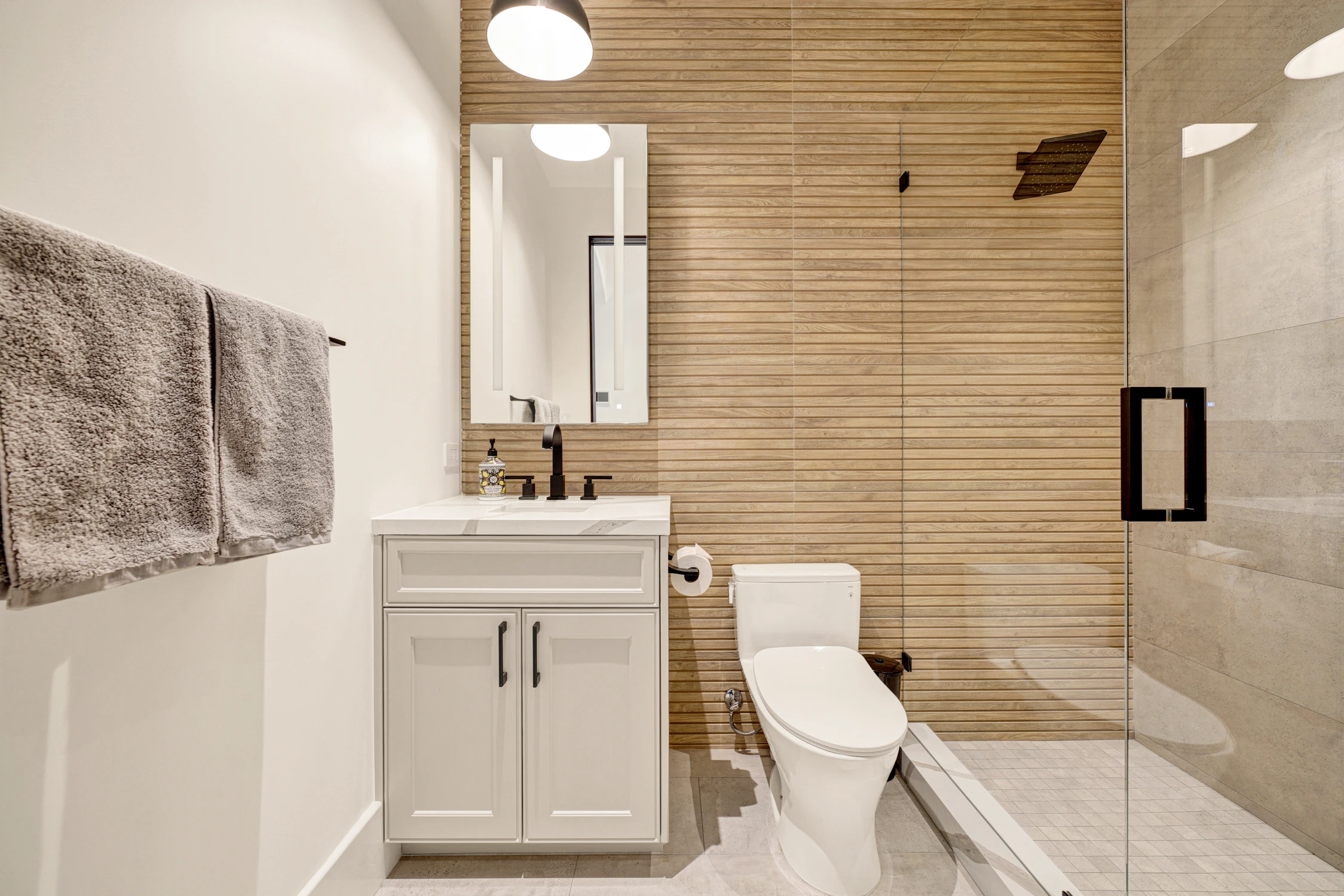 Bathroom with white vanity, glass shower, and wood-look tile wall