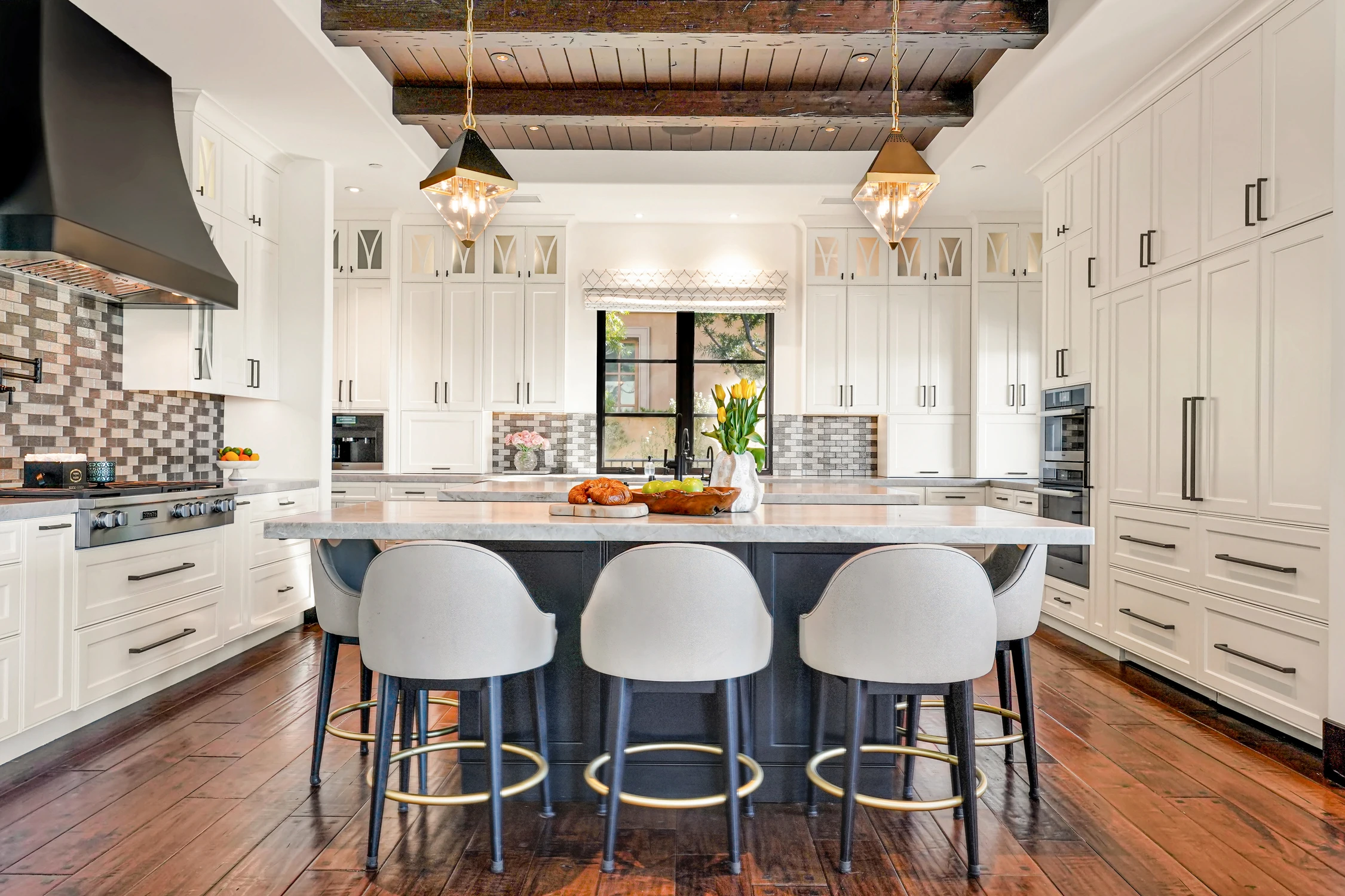 White kitchen with dark island, wood beams, and bar stools