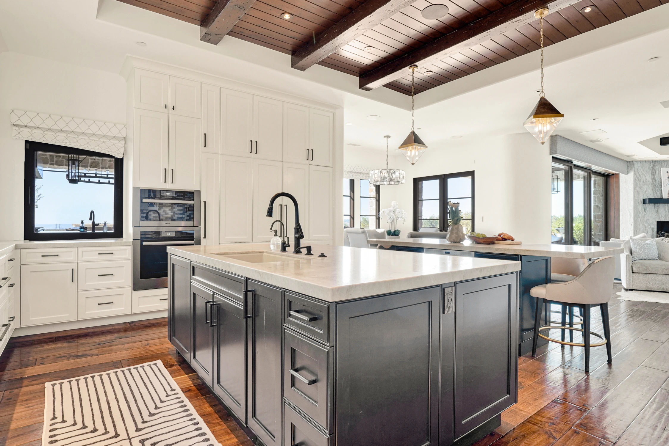 Kitchen with dark island and white cabinetry beneath wood beams