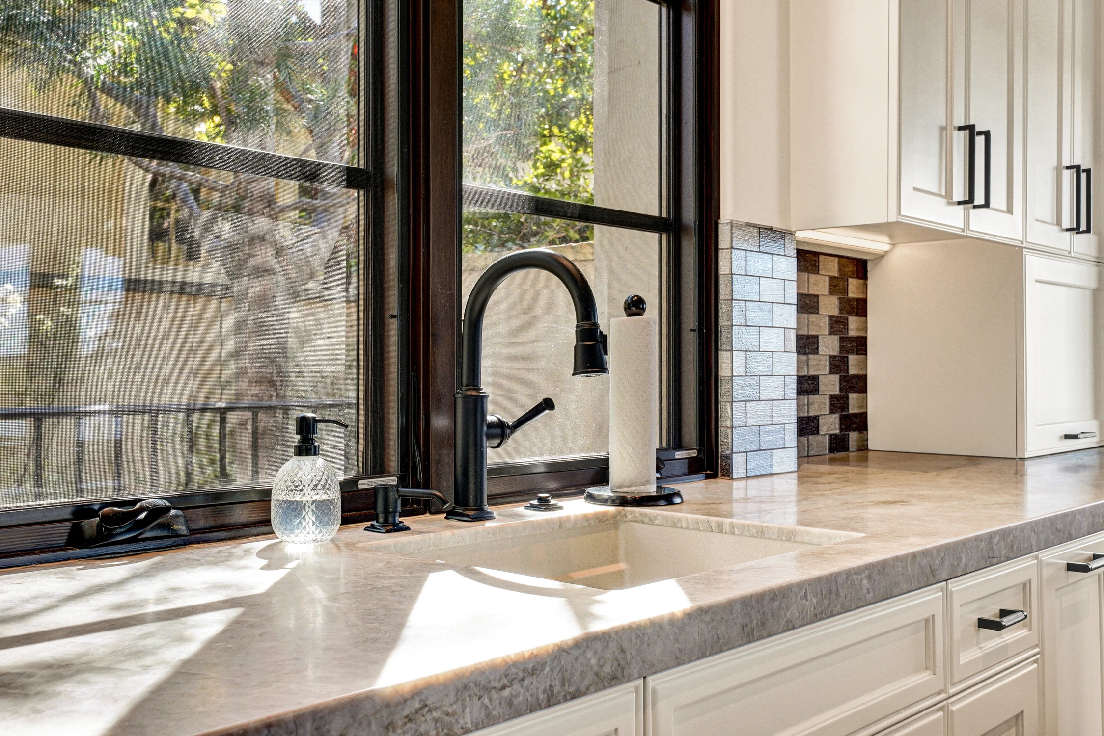Black kitchen faucet beside window and mosaic tile backsplash