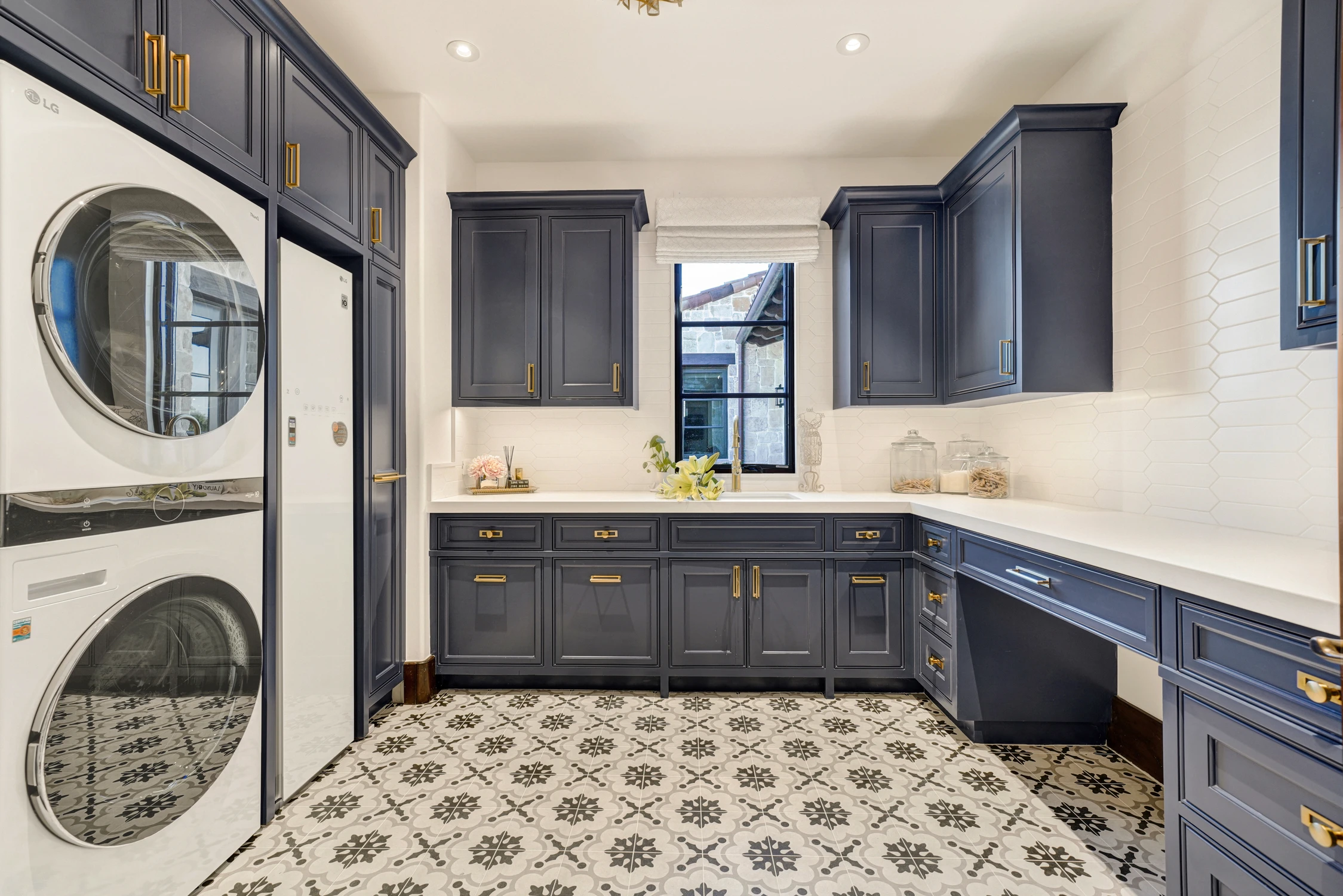 Laundry room with navy cabinetry, patterned tile floor, and stacked appliances