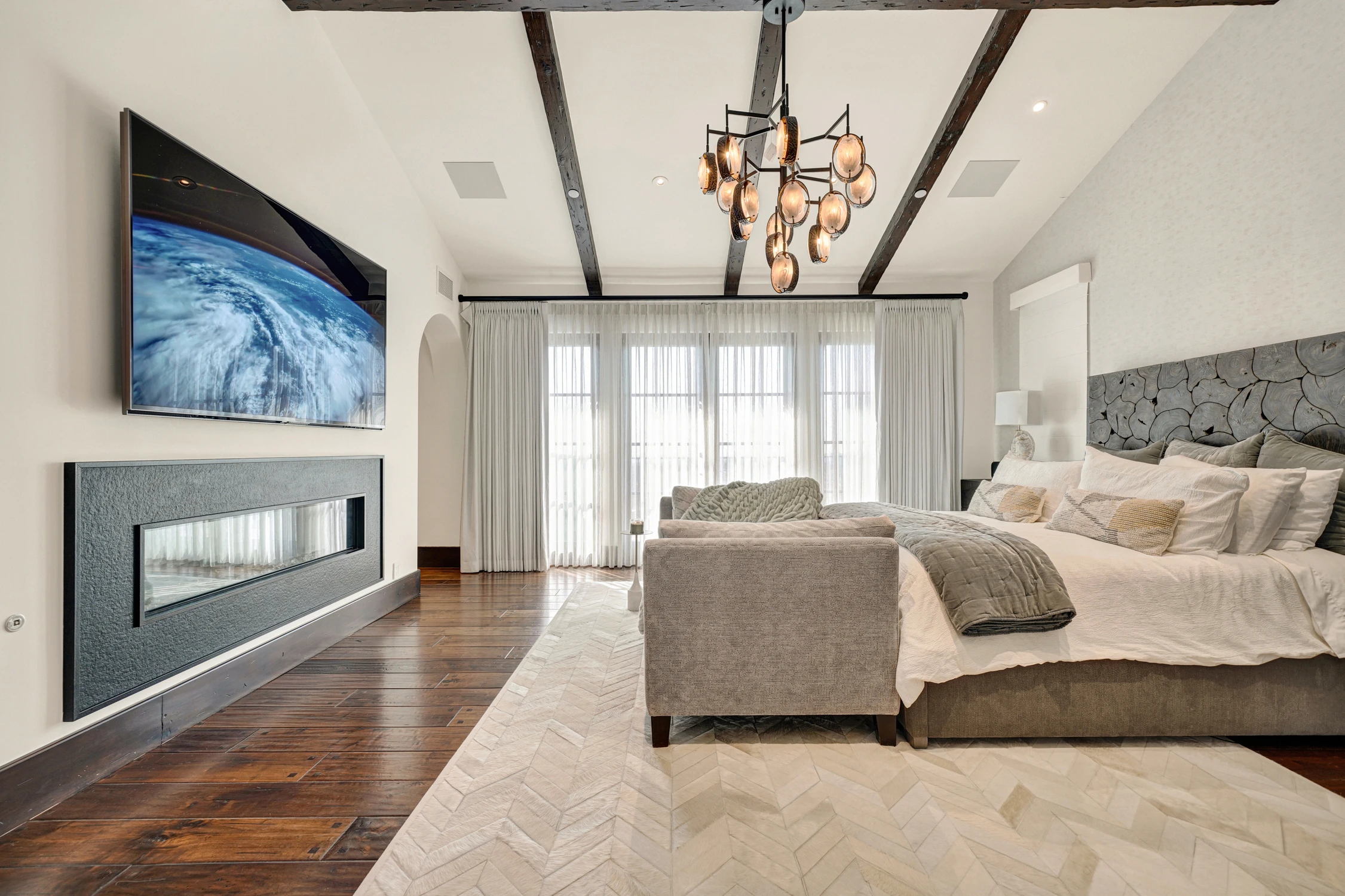 Primary bedroom with gray upholstered bed, dark wood beams, and fireplace