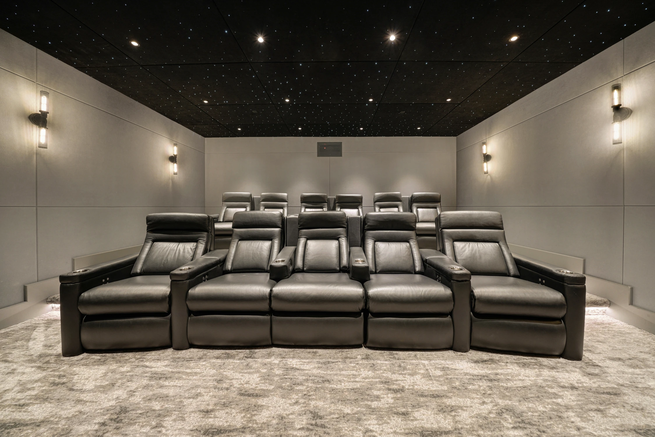 Home theater with rows of black recliners and wall sconces