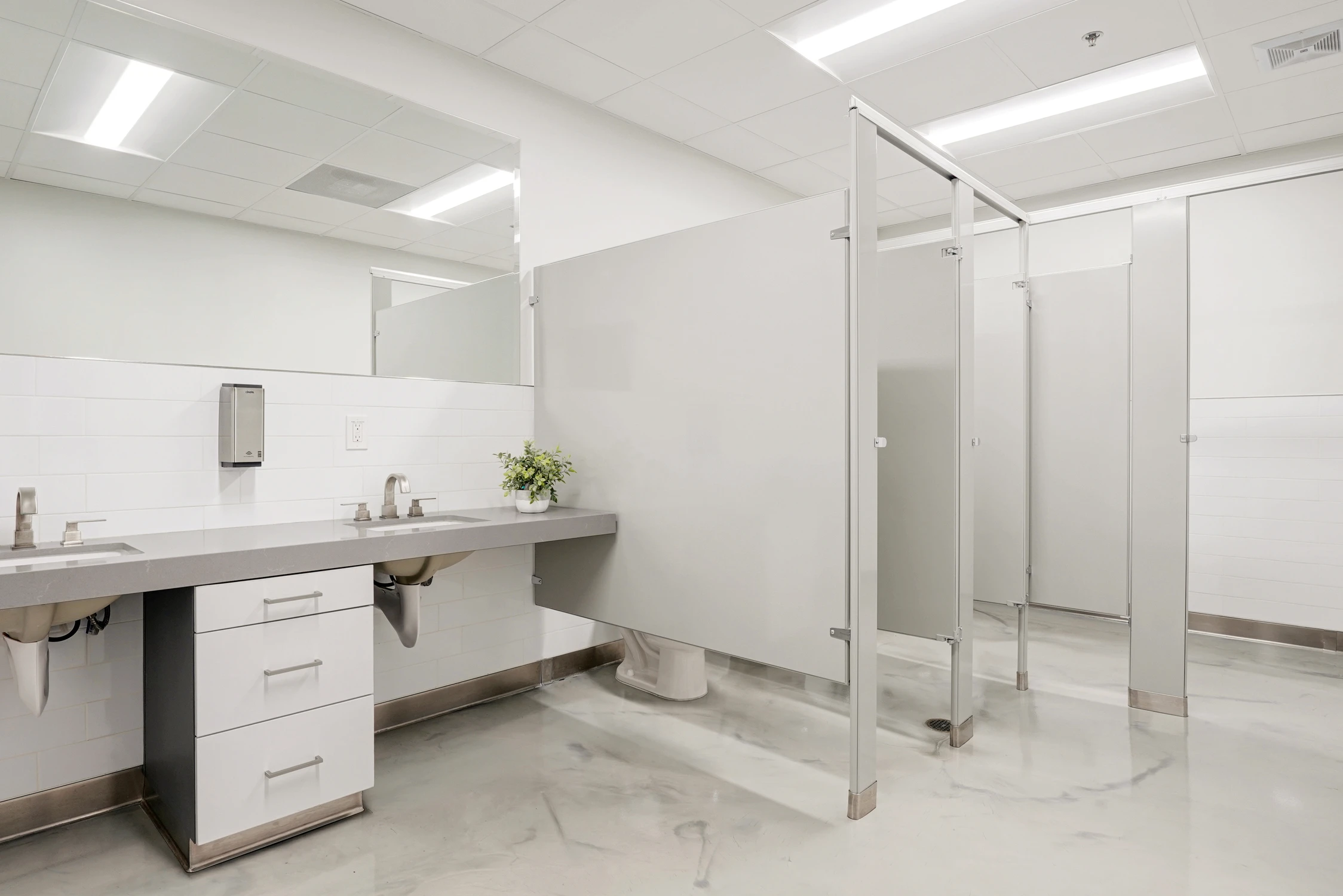 Commercial restroom with white tile walls and partitioned stalls