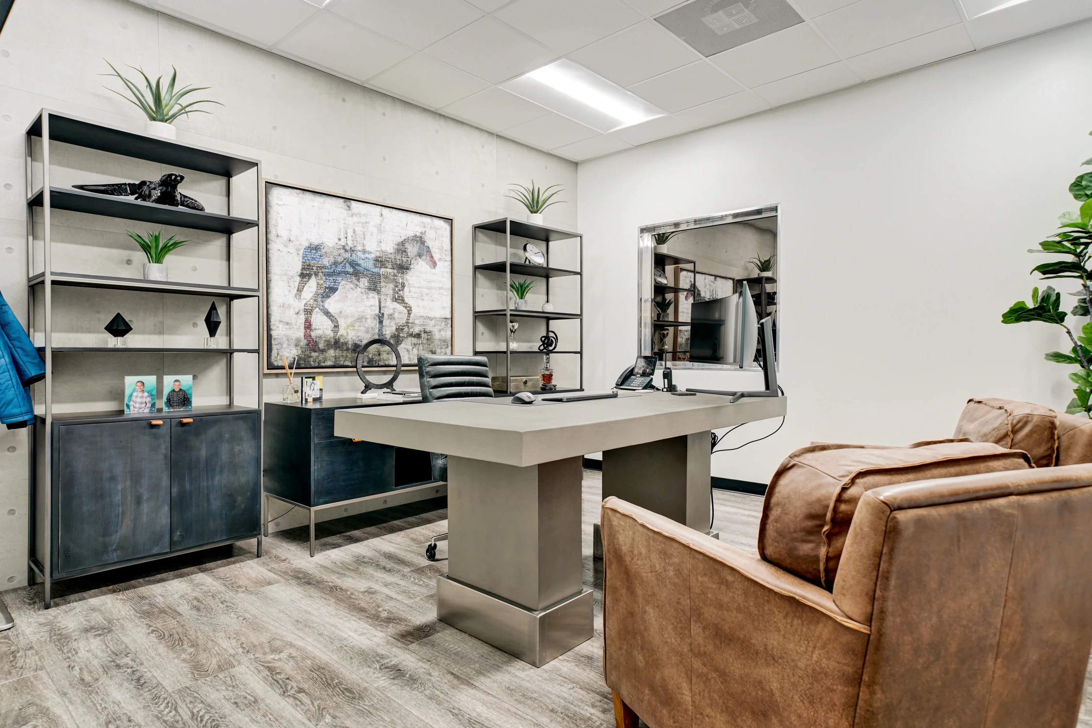 Office with concrete walls, desk, shelving, and leather guest chairs