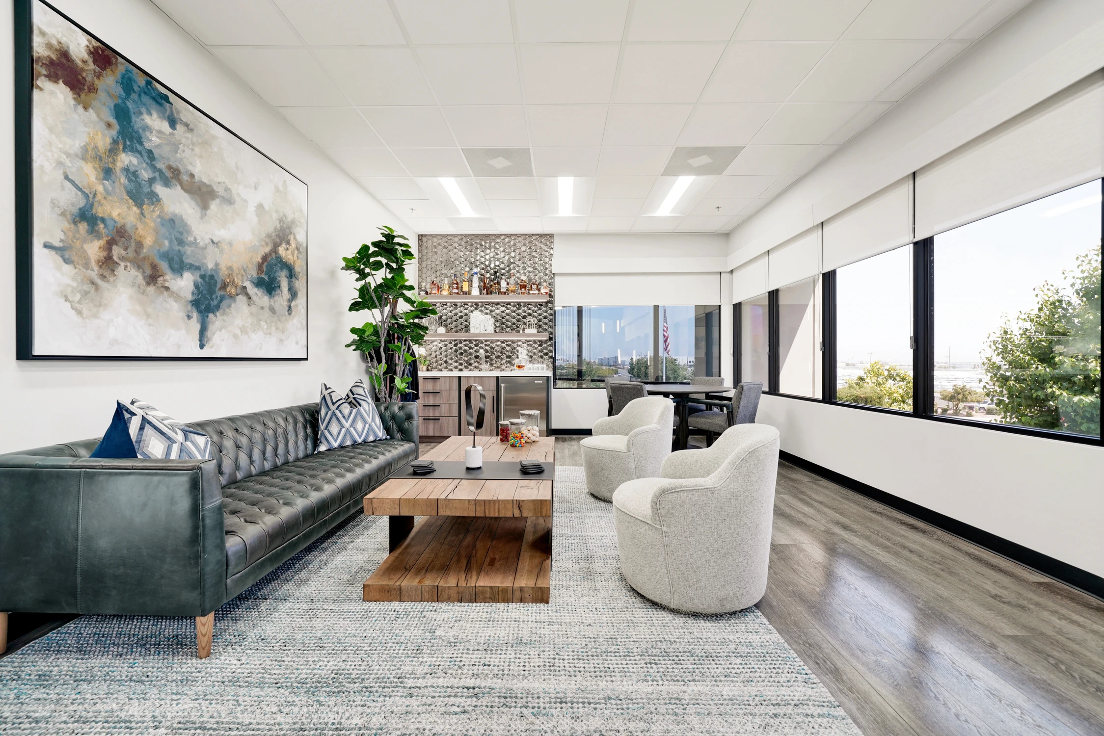 Executive office seating area with dark tufted sofa, beverage bar, and windows