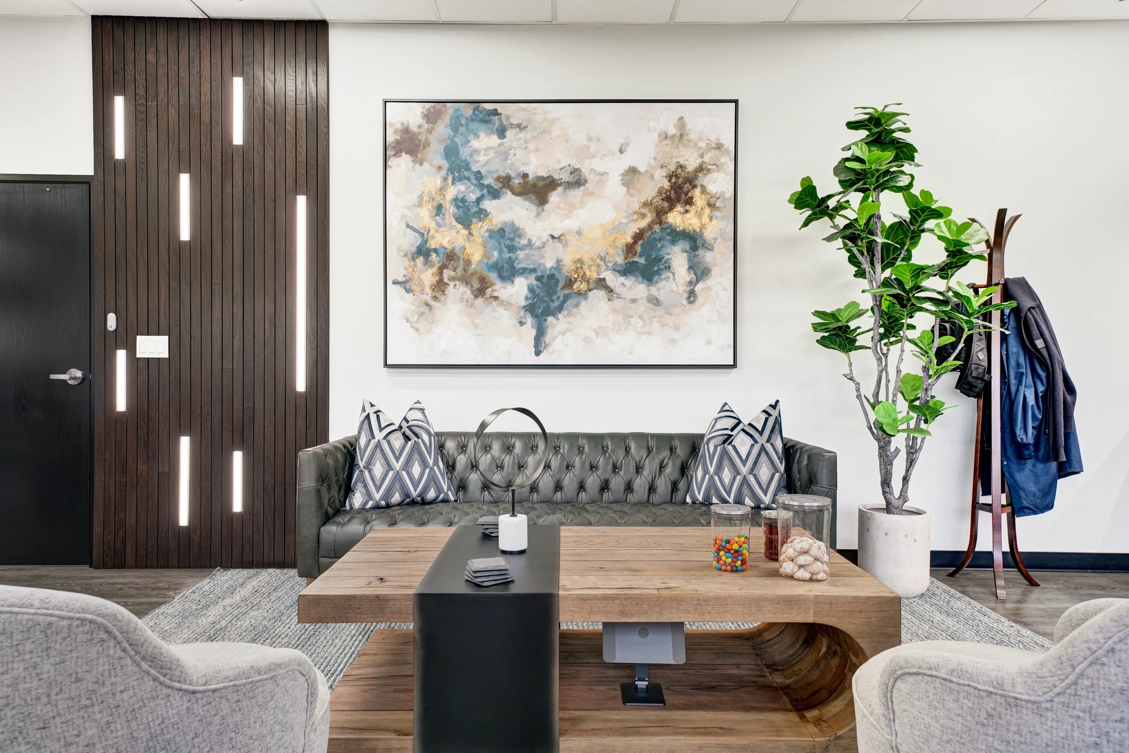 Executive office seating area with dark sofa, desk, and wood accent wall