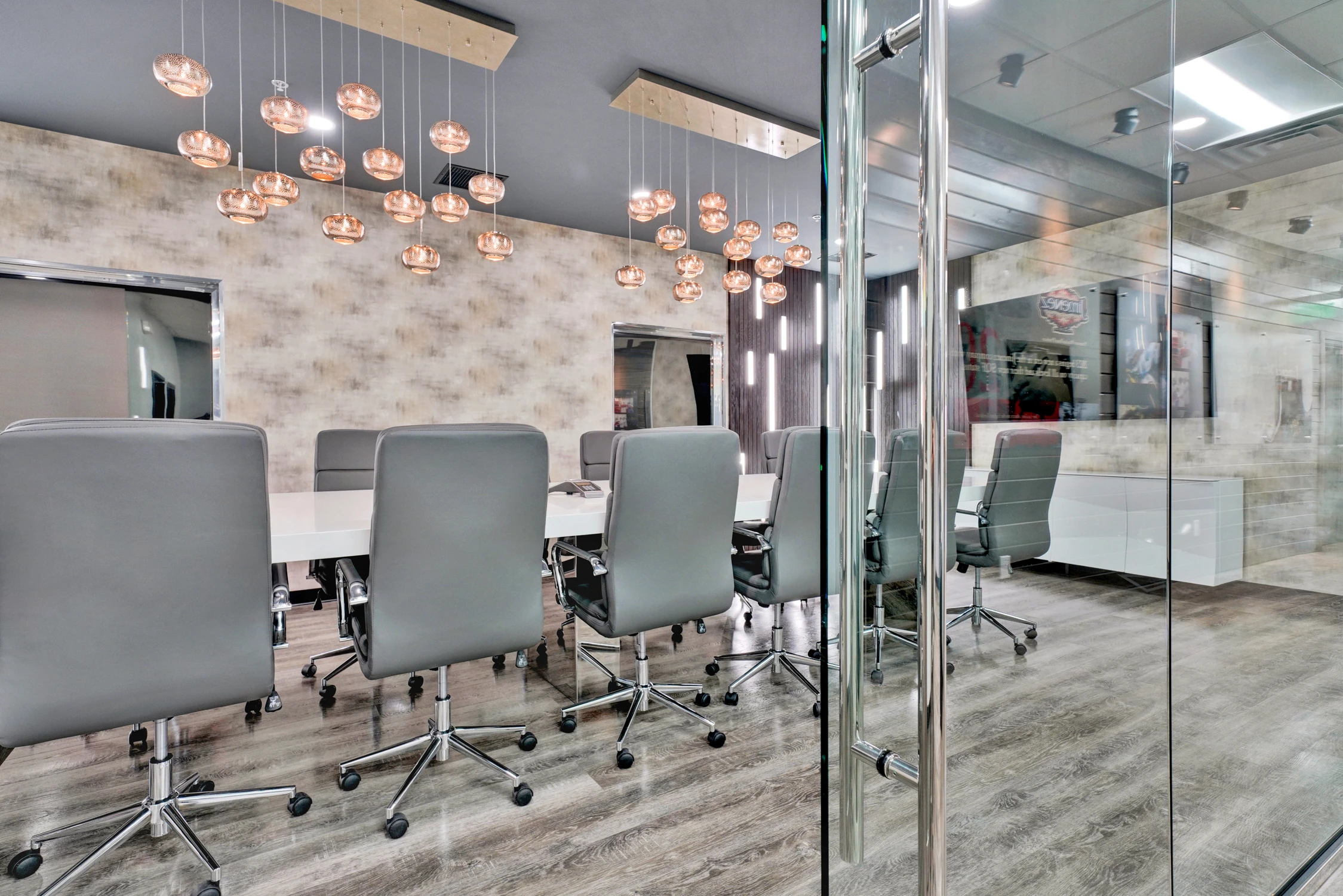 Conference room chairs beneath clustered glass pendants and wall monitor