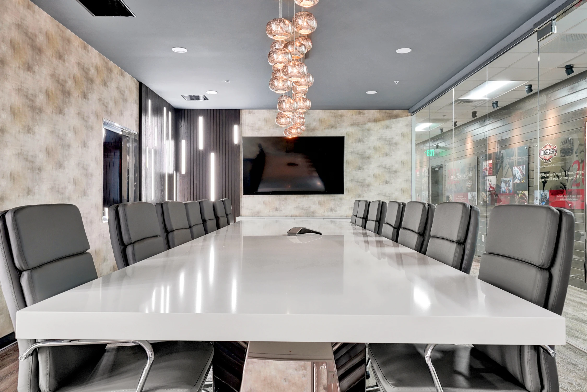 Conference table facing wall monitor and glass-walled office corridor