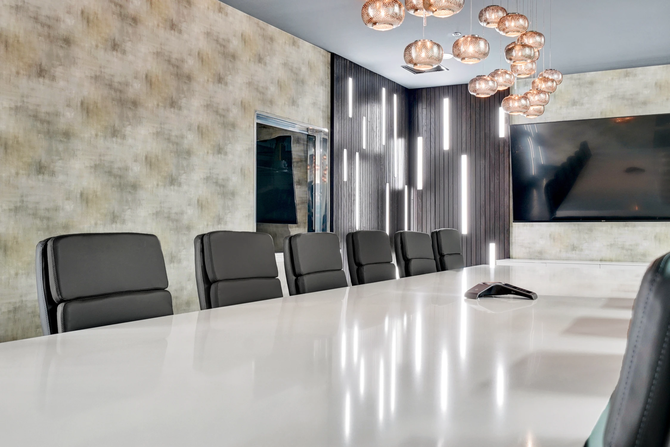 White conference table framed by pendant lights and illuminated wood wall