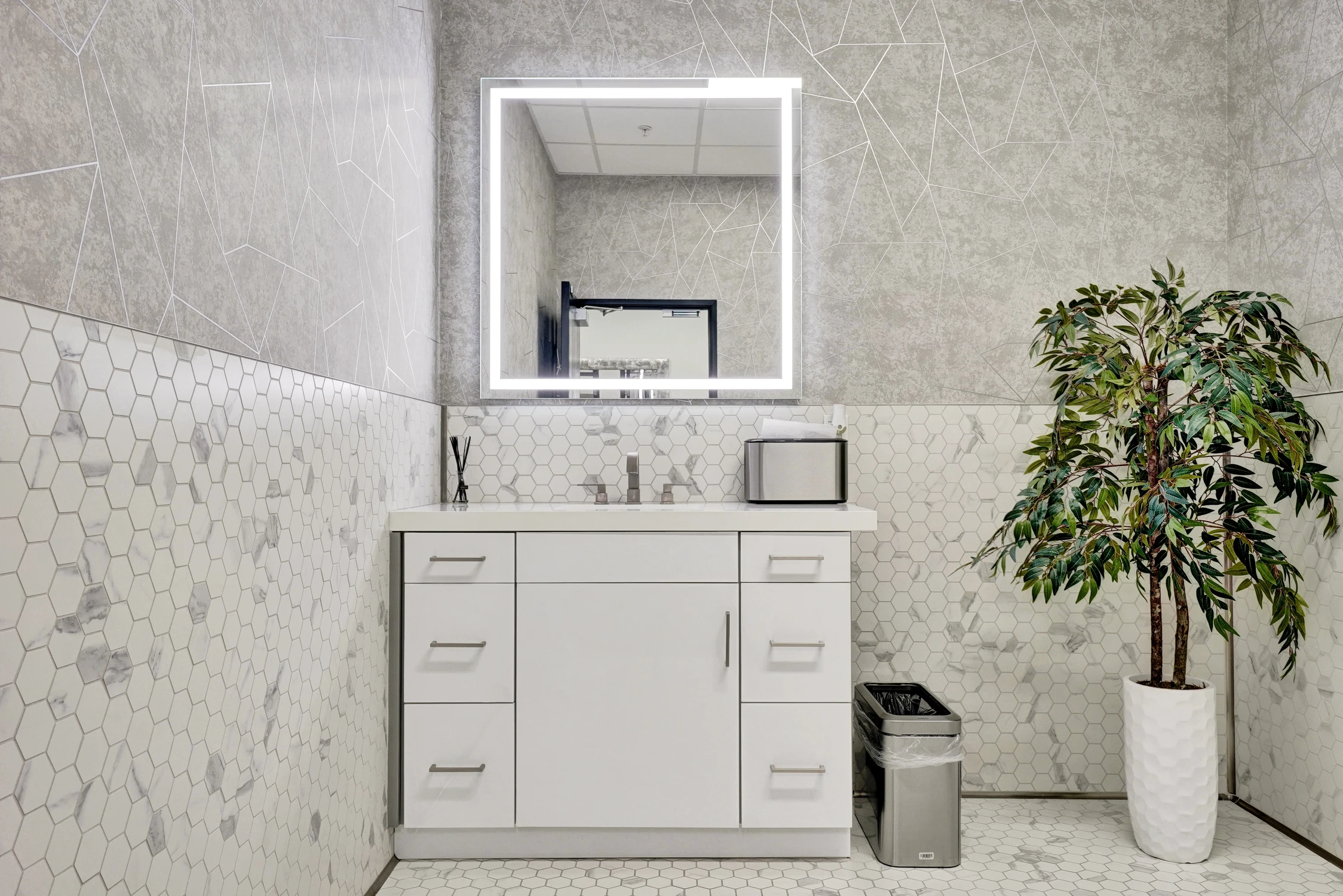 Commercial restroom vanity with hexagonal tile backsplash and illuminated mirror