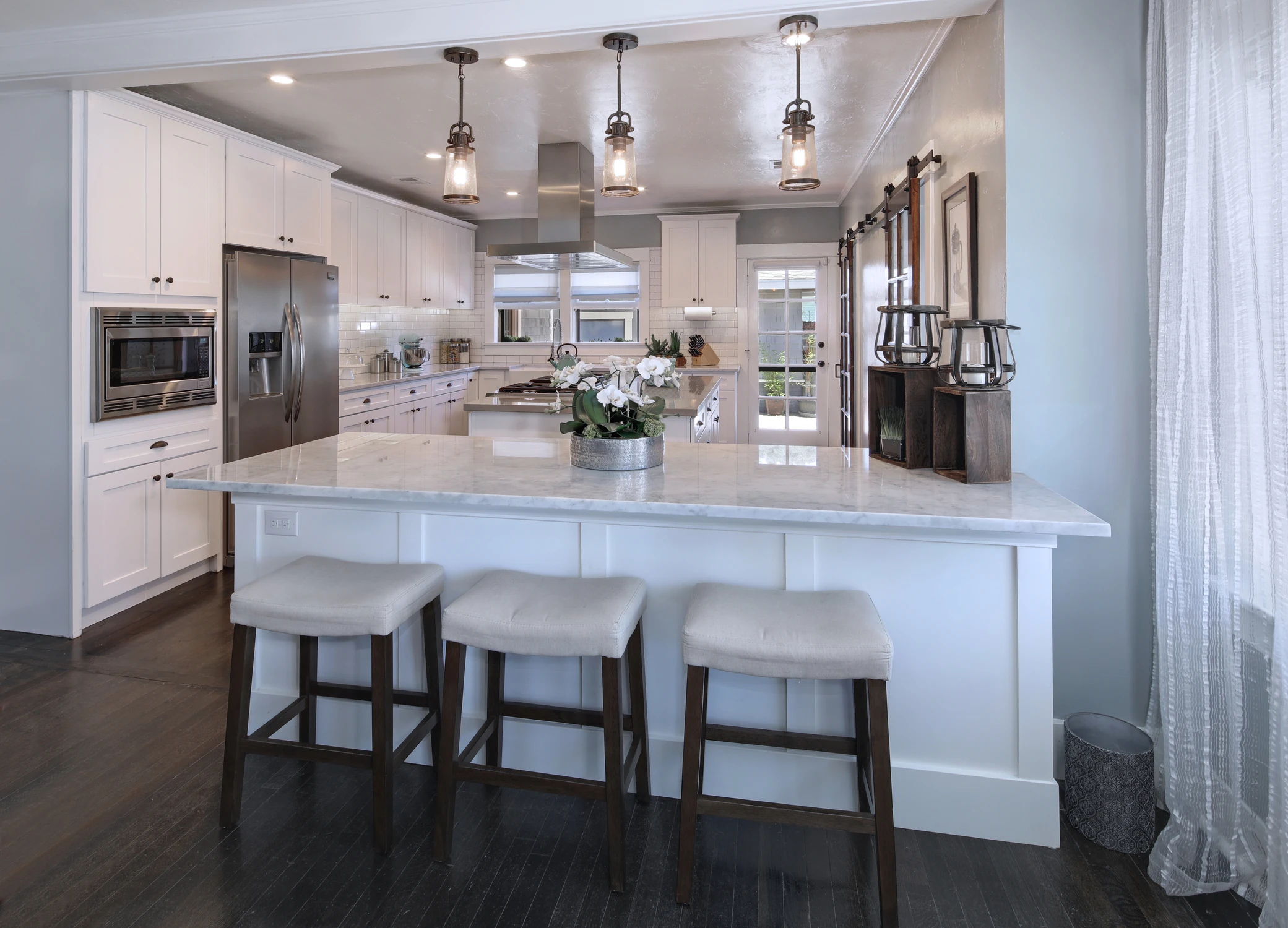 White kitchen island with four stools and stainless steel range hood