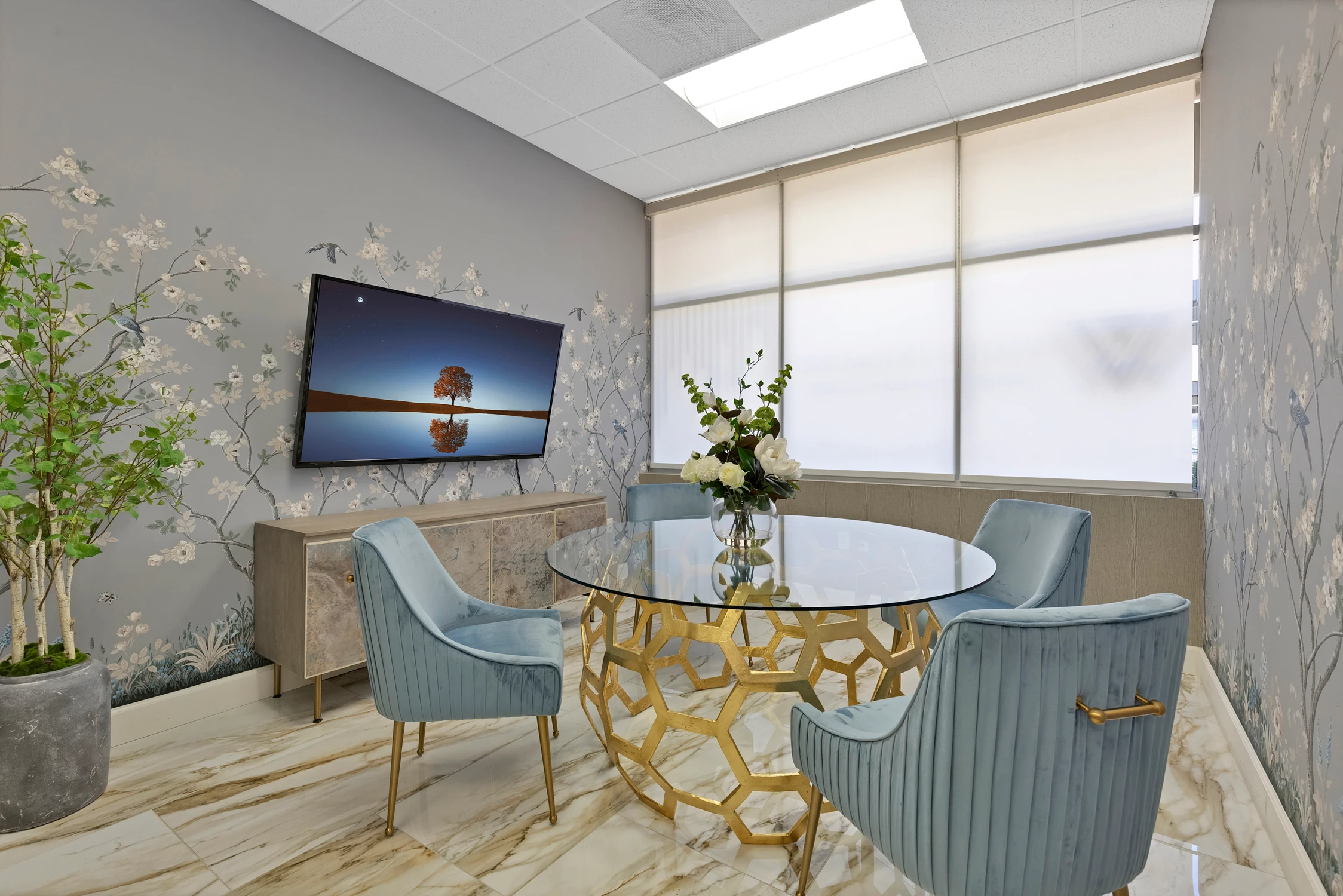 Meeting room with floral wallcovering, glass table, and blue velvet chairs