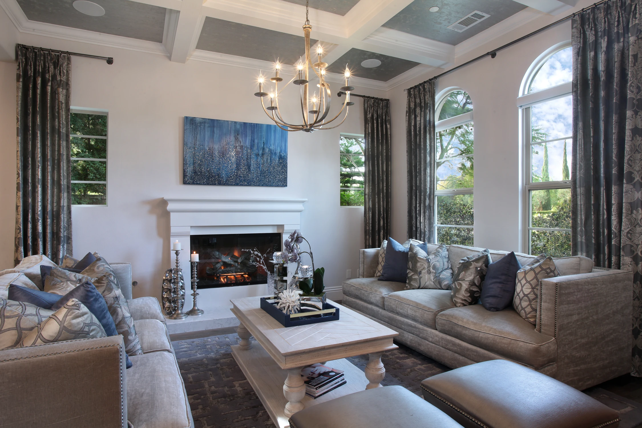 Formal living room with coffered ceiling, white fireplace, and blue-gray seating
