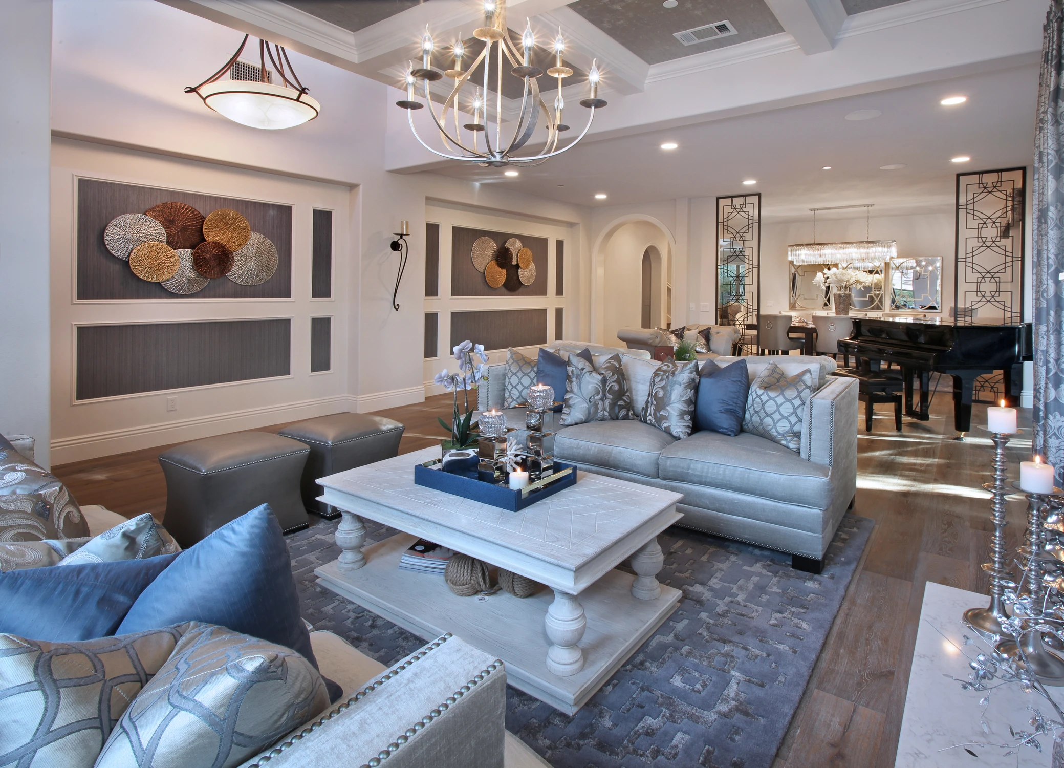Open living room with pale sofas, chandelier, and dark kitchen beyond
