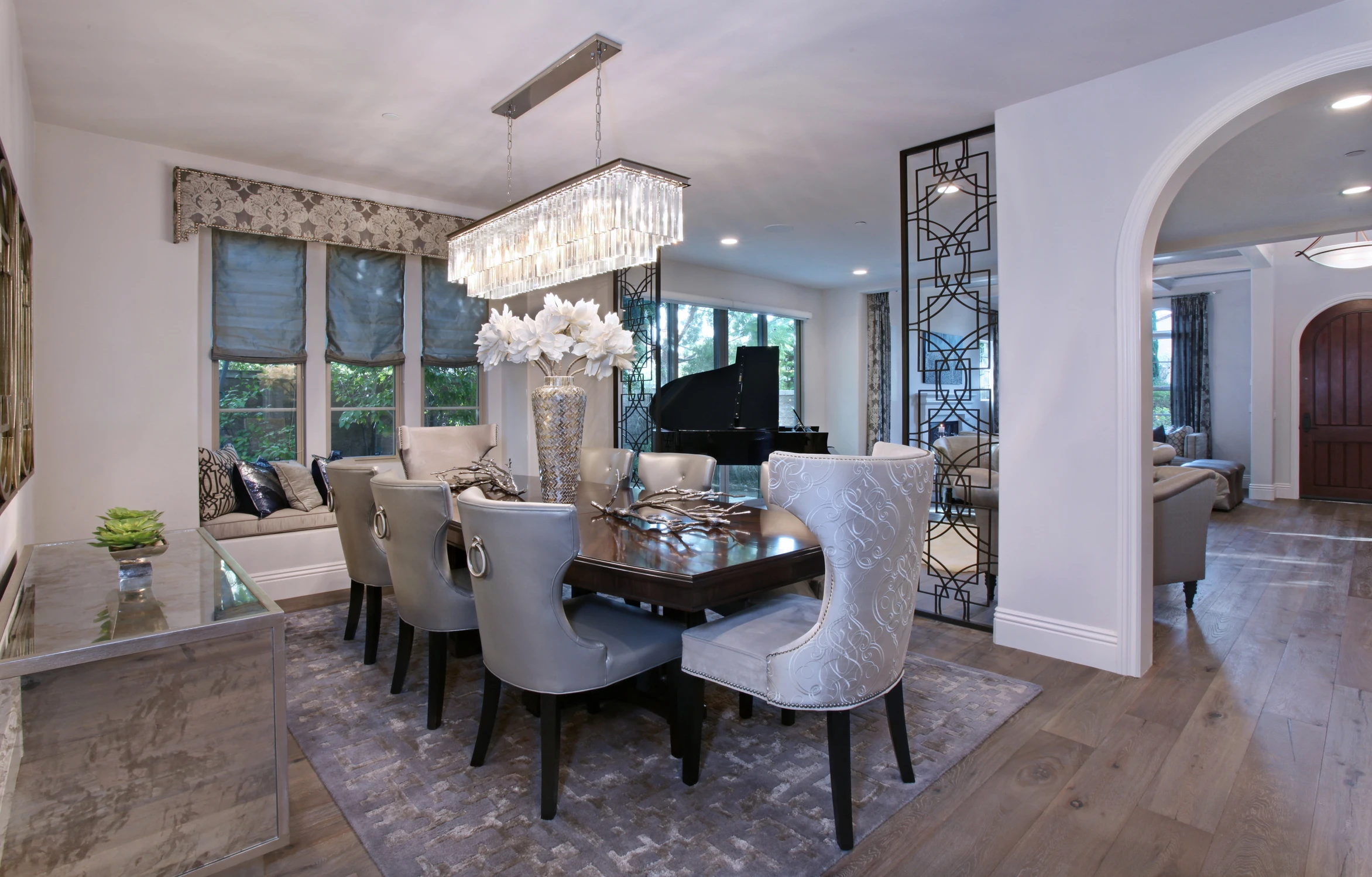 Formal dining room with crystal chandelier, pale chairs, and arched opening