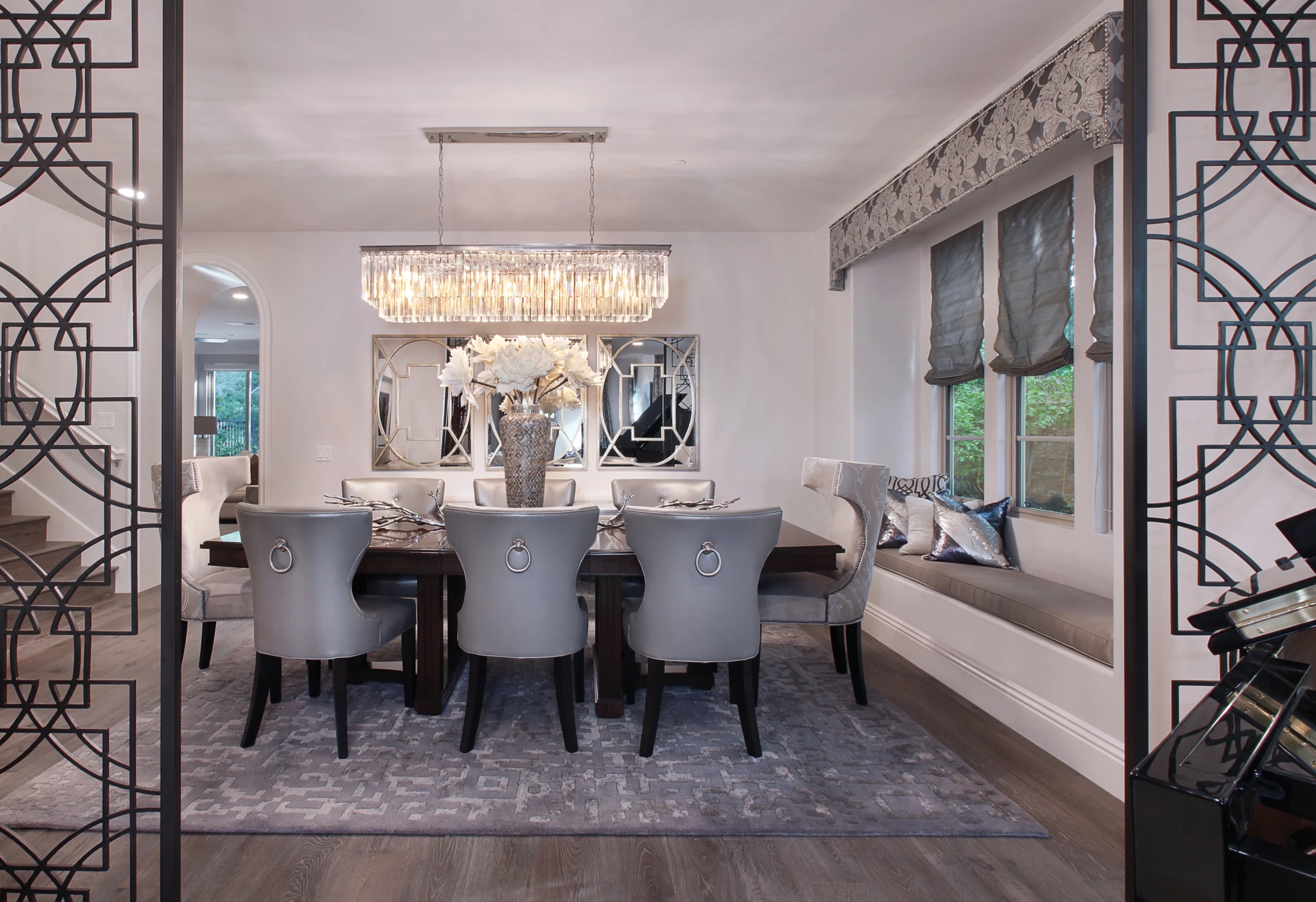 Dining table with upholstered chairs beneath layered crystal lighting