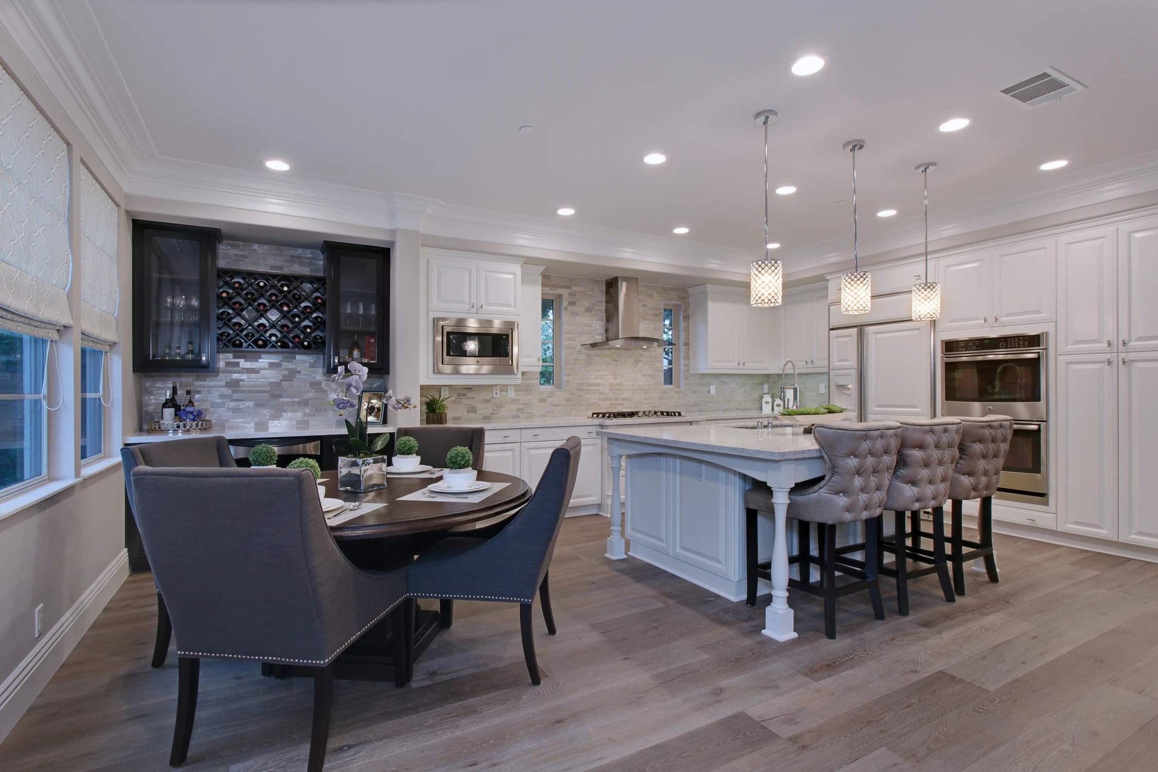 White kitchen with central island, dark dining chairs, and recessed lighting