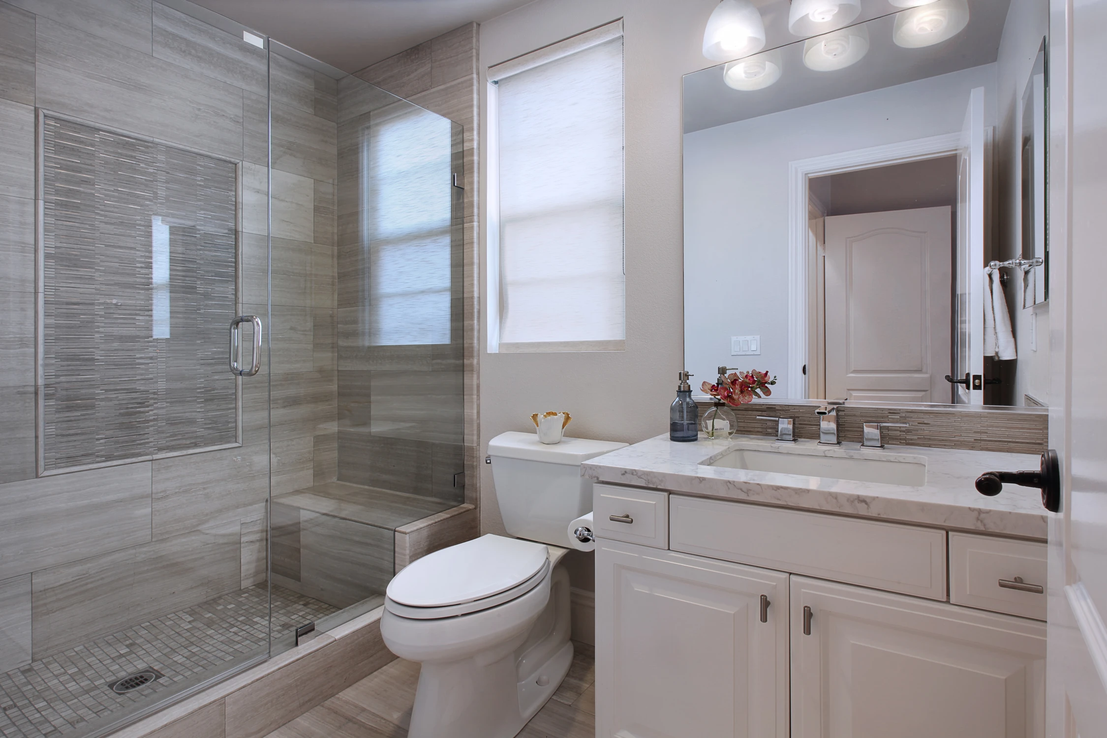 Bathroom with glass shower, white vanity, and neutral tile walls
