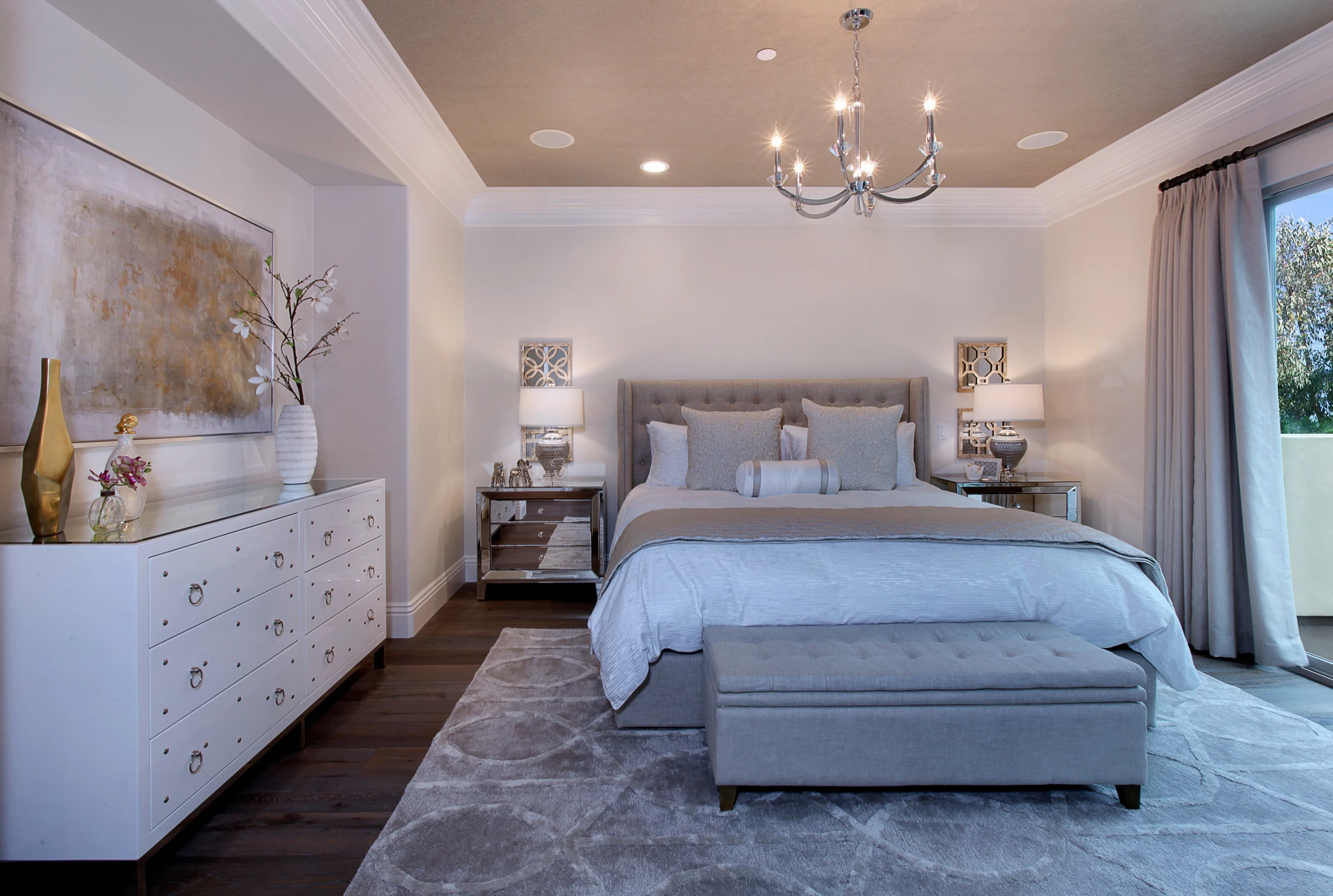 Master bedroom with gray upholstered bed, pale blue bench, and glass doors