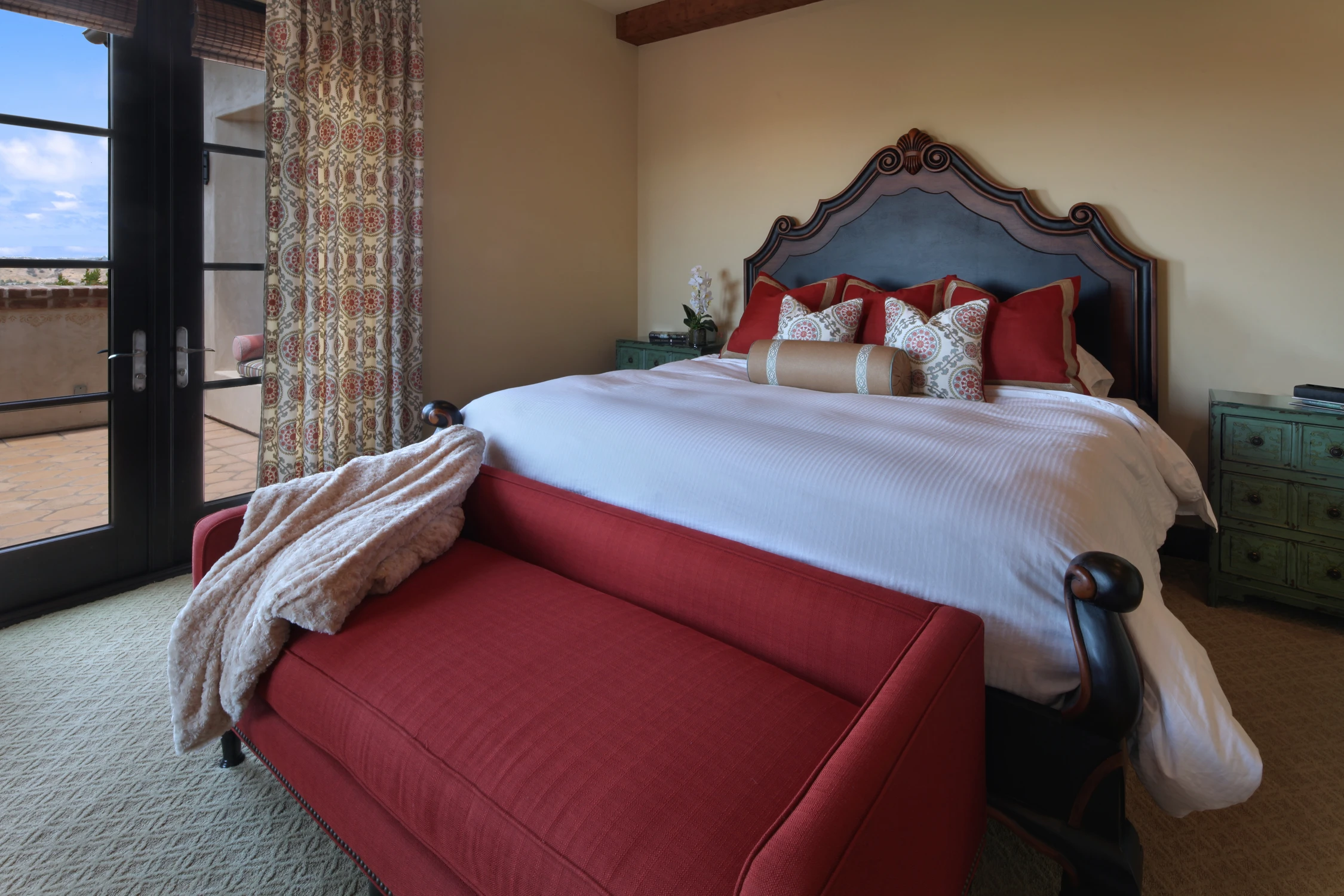 Bedroom with carved dark wood bed, red bench, and balcony doors