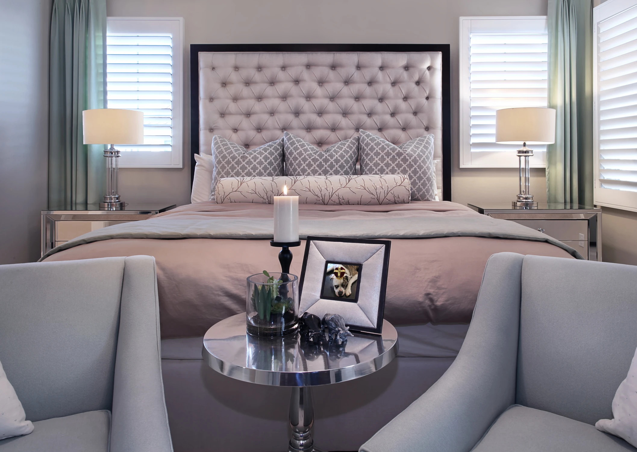 Bedroom with tall tufted headboard, pale green chairs, and crystal chandelier