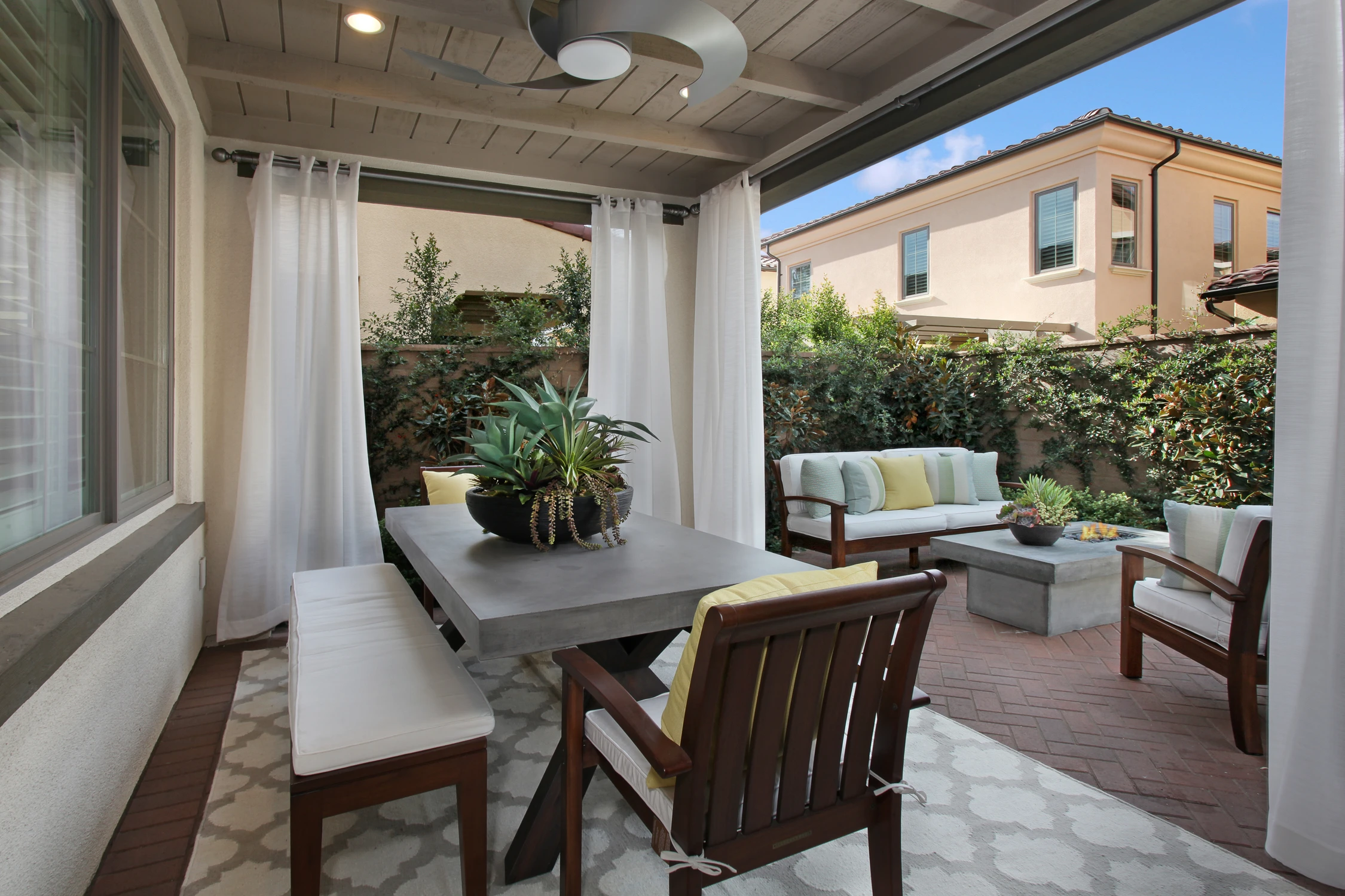 Covered outdoor dining area with wood table and pale cushioned seating