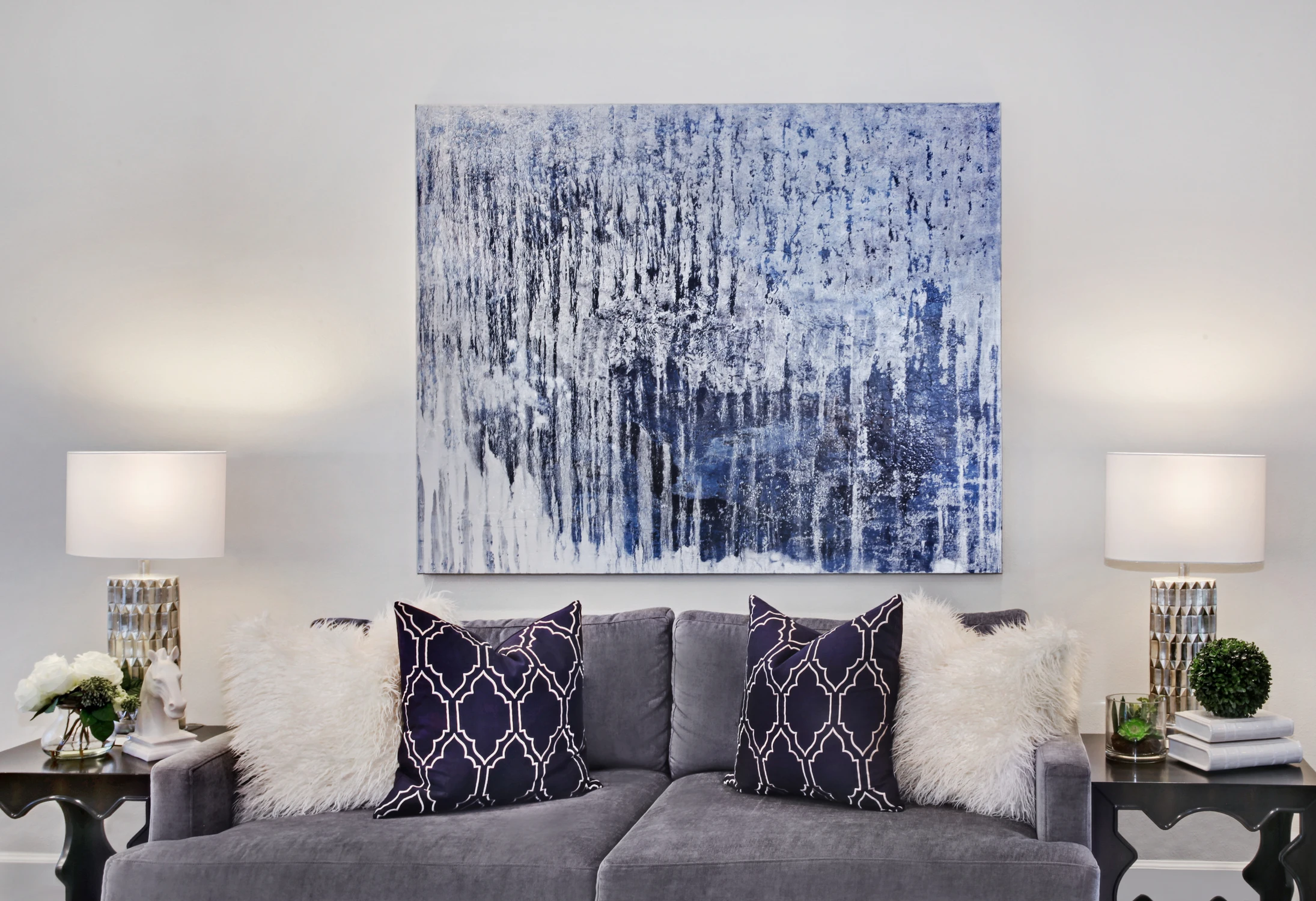 Gray sofa with navy patterned pillows beneath blue abstract artwork
