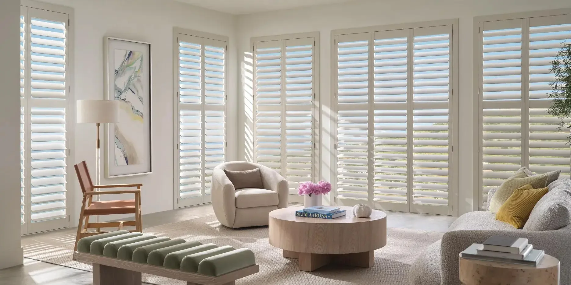 White plantation shutters across multiple windows in a sunlit living room