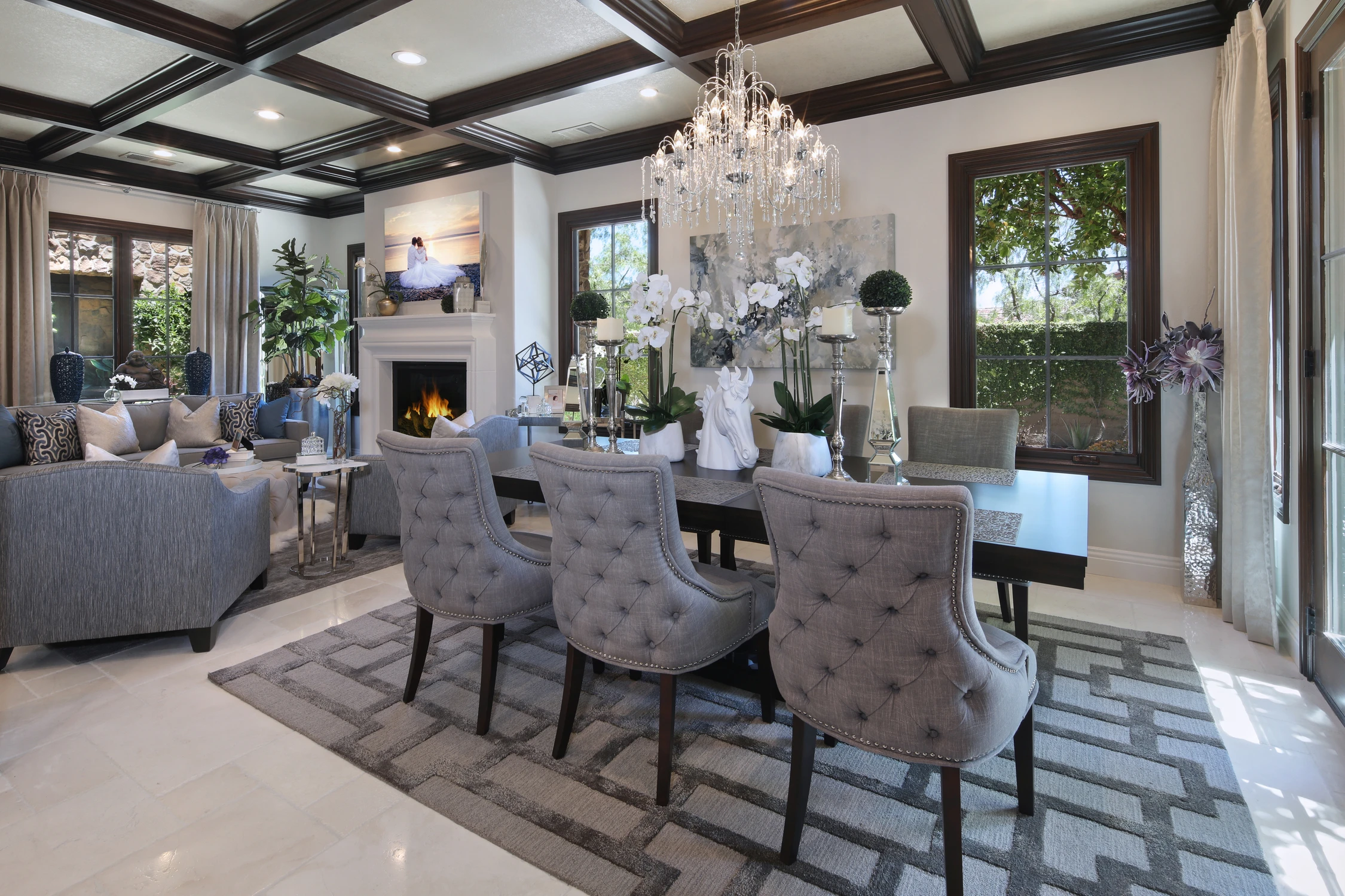 Open living and dining room with gray seating, dark beams, and chandelier