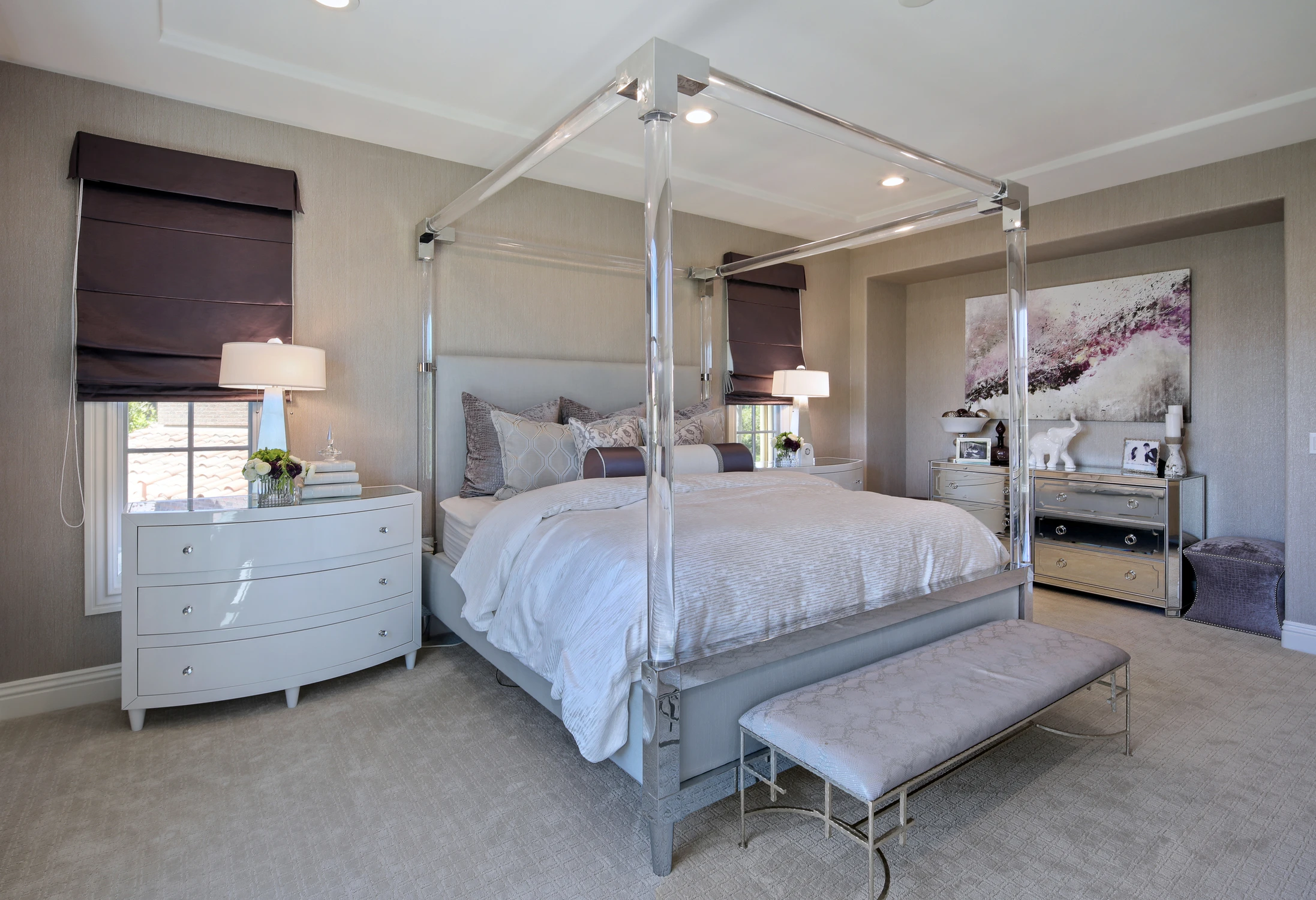 Primary bedroom with acrylic poster bed, metal accents, mirrored furniture, and purple window treatments
