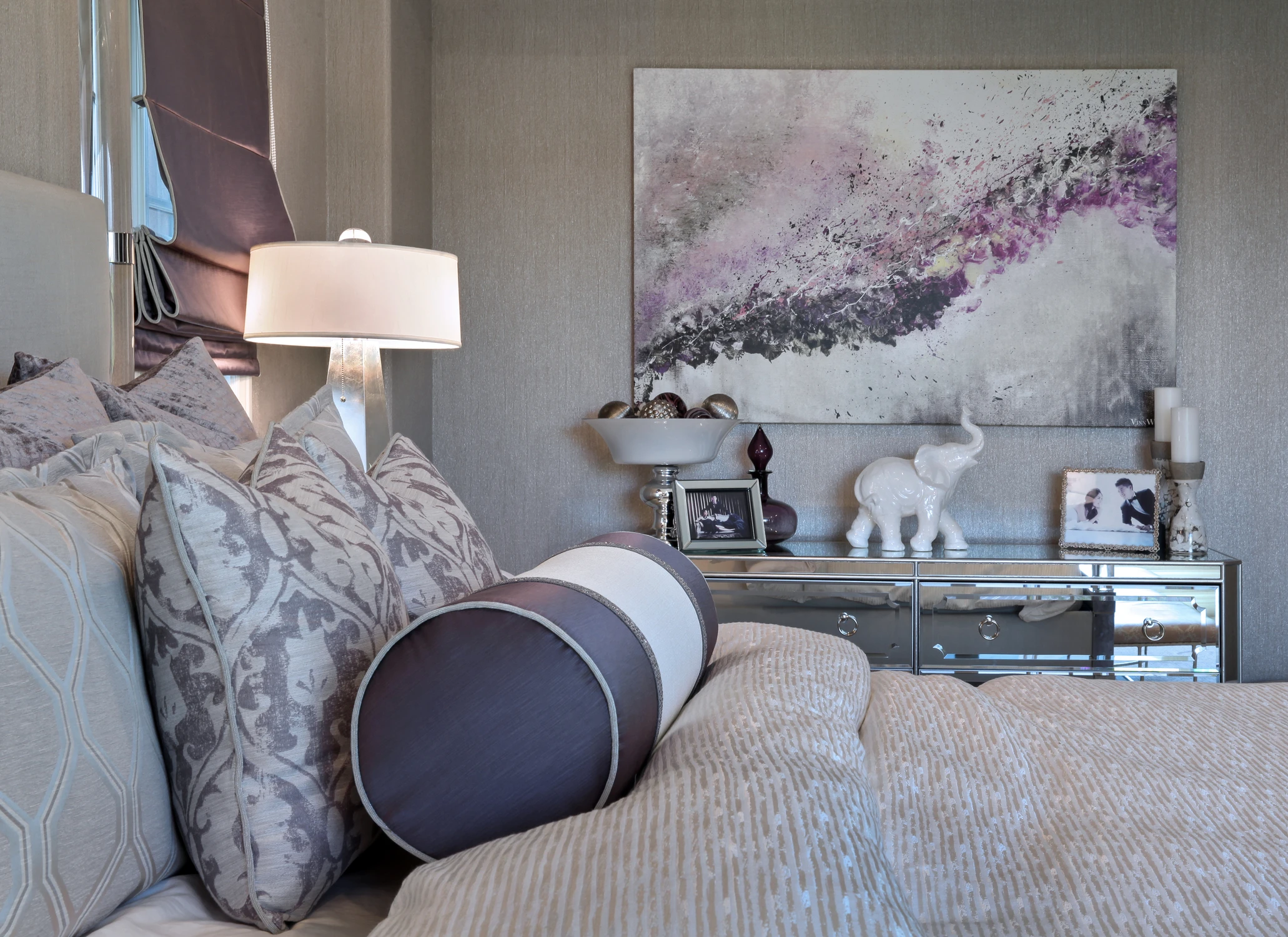 Bedroom with patterned pillows, mirrored dresser, and purple abstract artwork