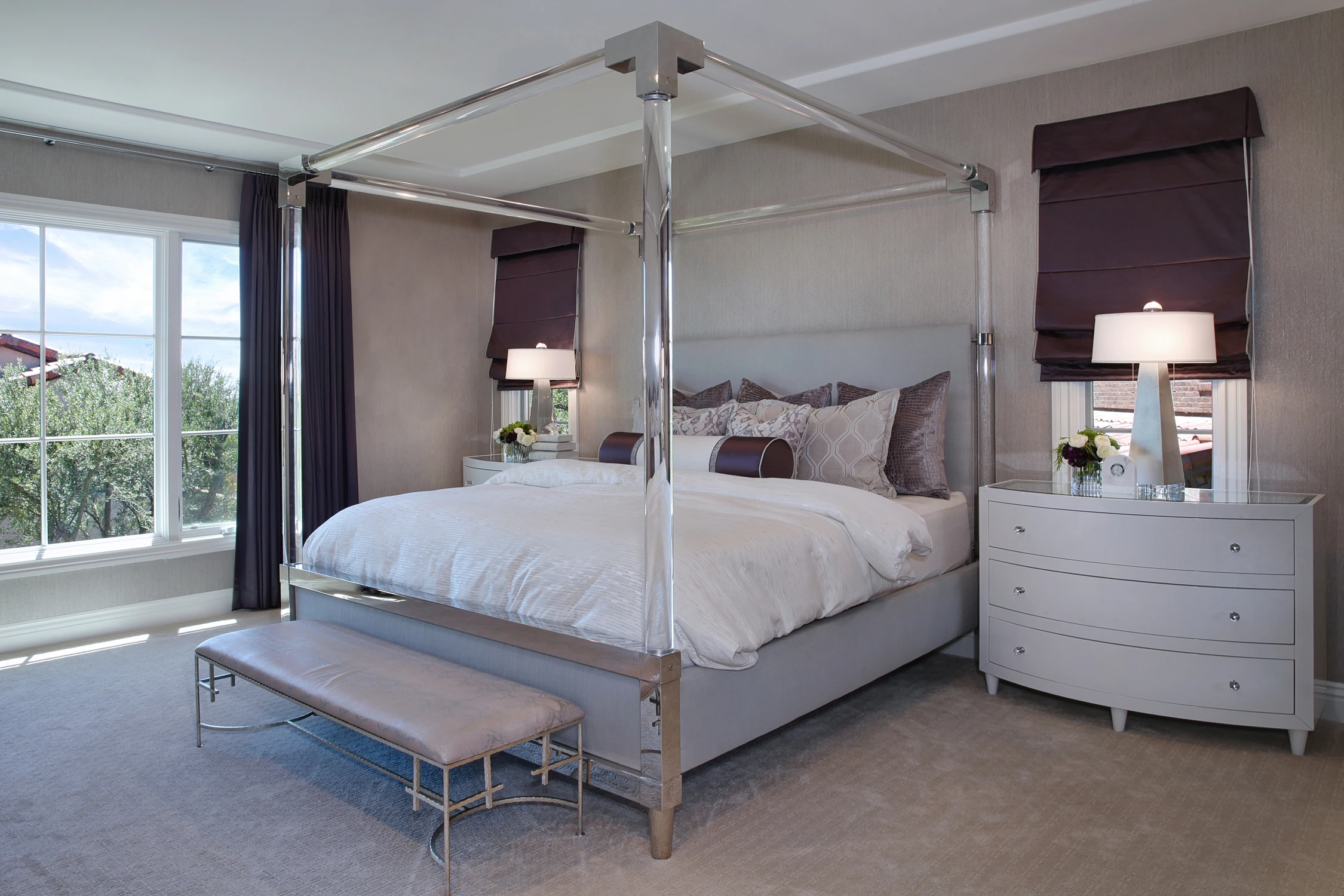Primary bedroom with acrylic poster bed, metal accents, purple window treatments, and white nightstand