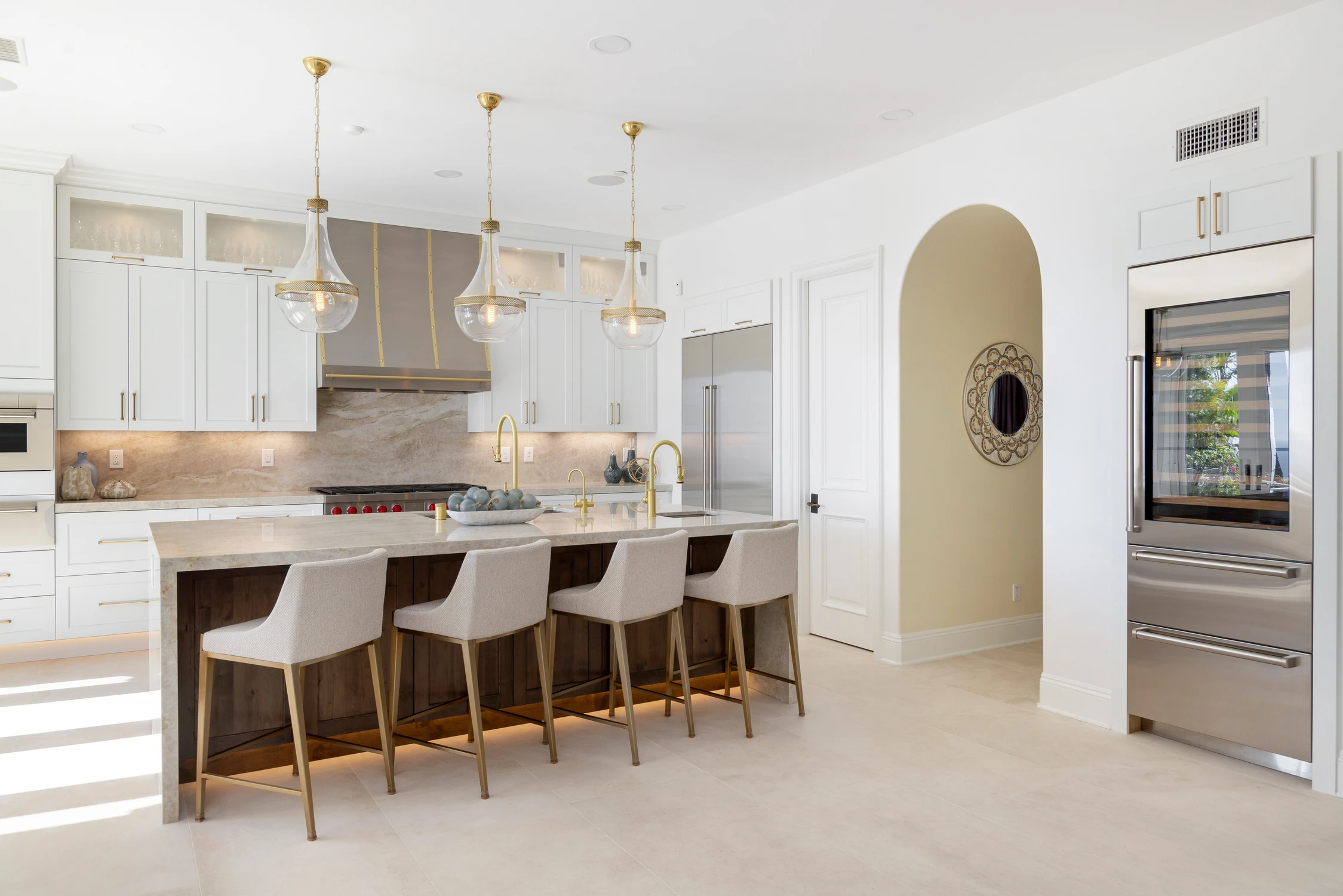 White kitchen with long wood island, brass pendants, and arched doorway