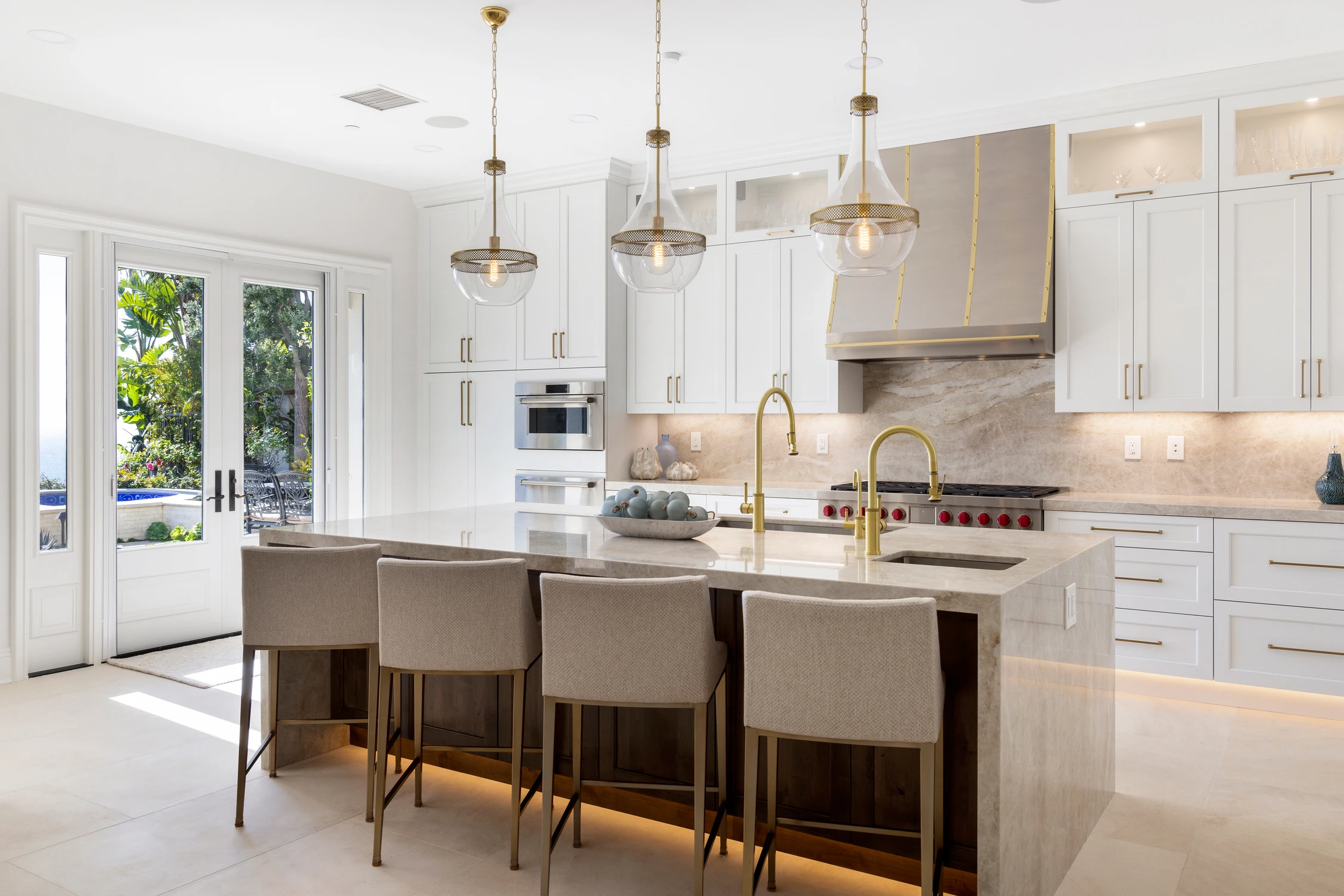 White kitchen island with wood paneling and row of brass pendant lights