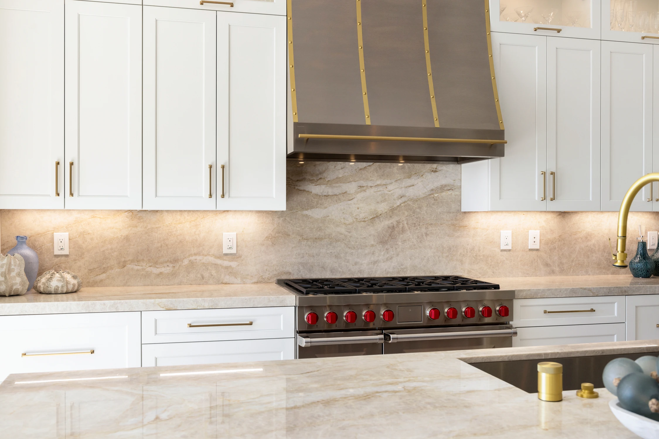 Kitchen range with stainless hood, white cabinets, and pale stone backsplash