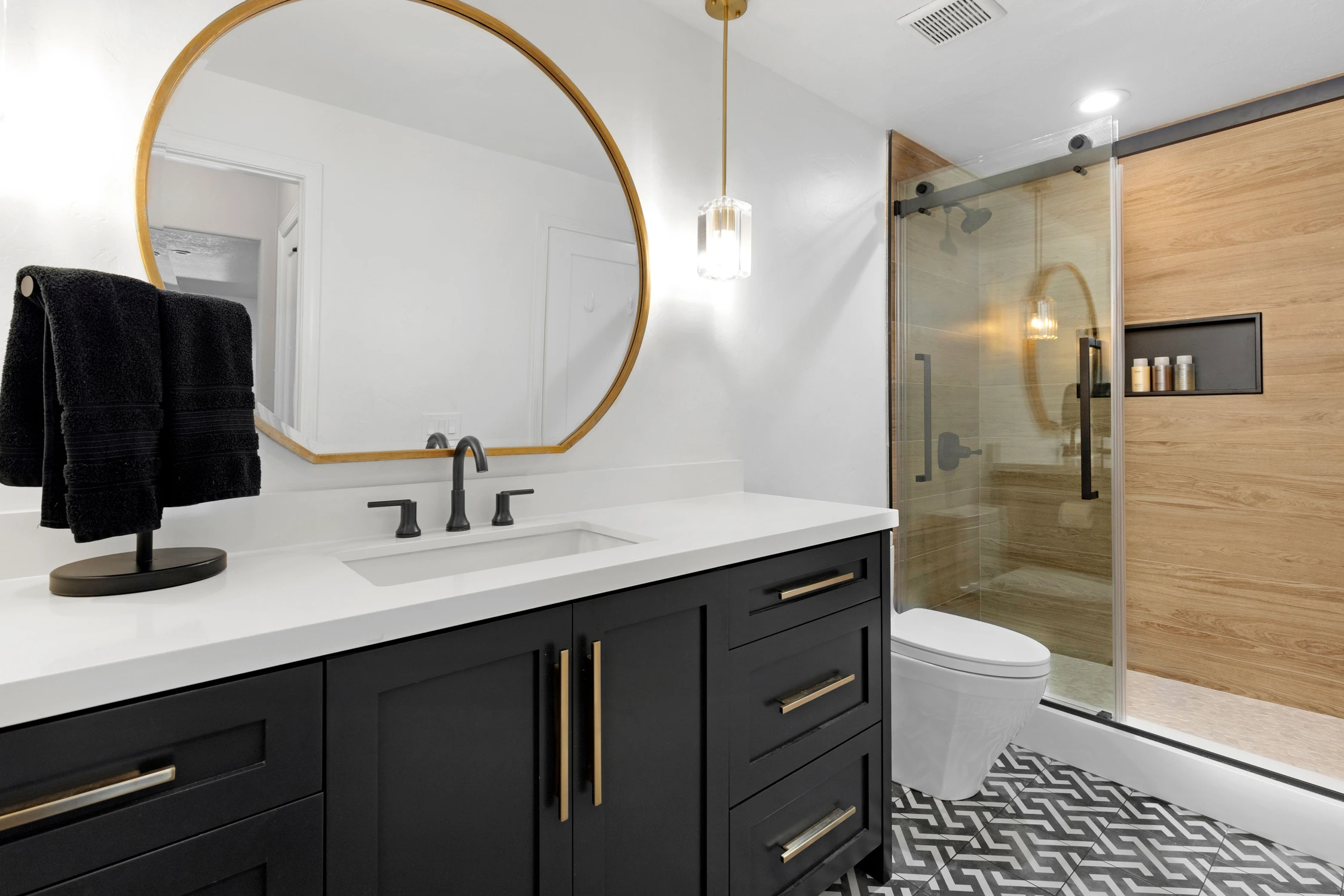 Bathroom vanity with dark drawers, round brass mirror, and patterned floor tile