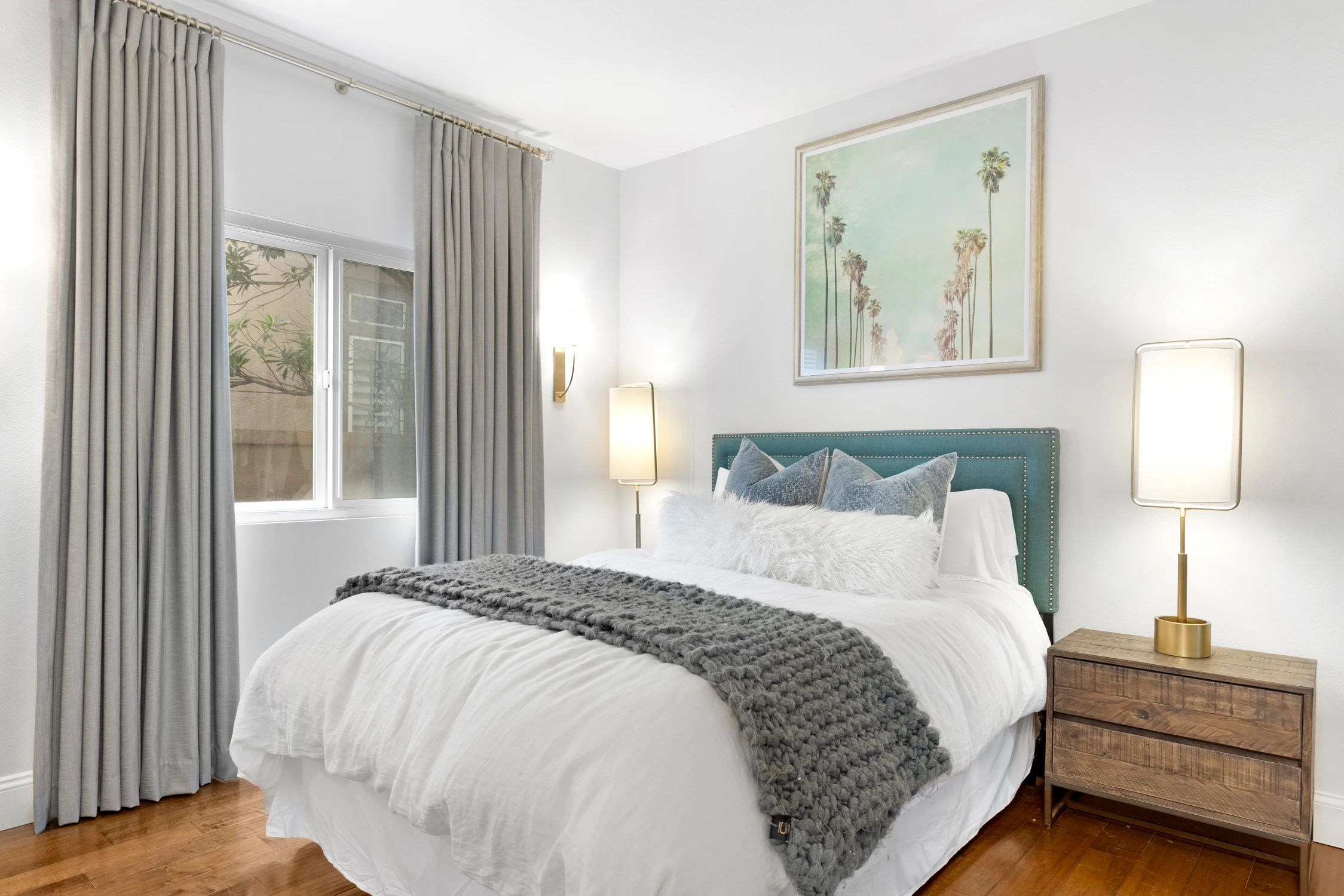 Bedroom with teal upholstered bed, pale artwork, and gray drapery