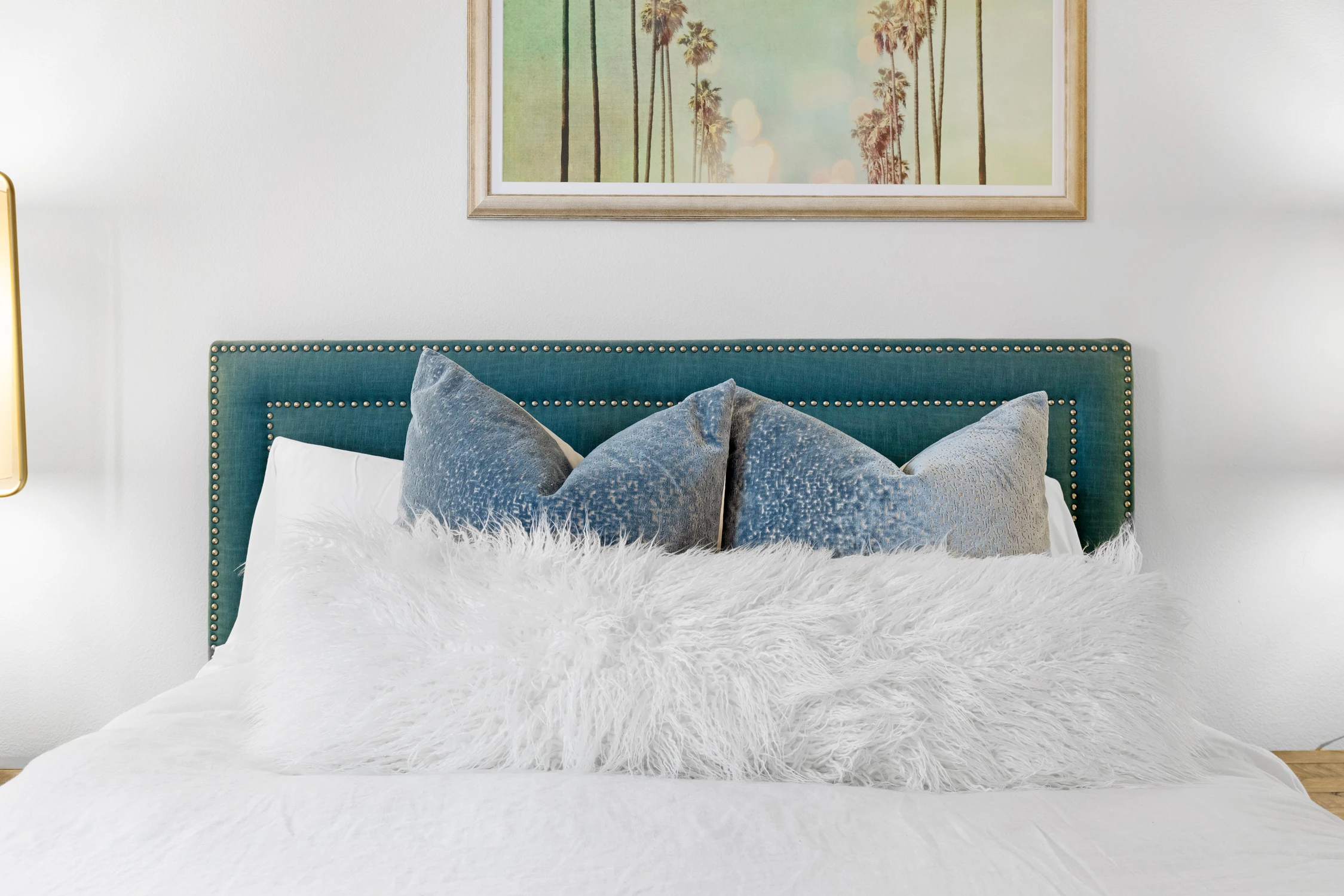 Bedroom bed detail with teal headboard, blue pillows, and pale framed art