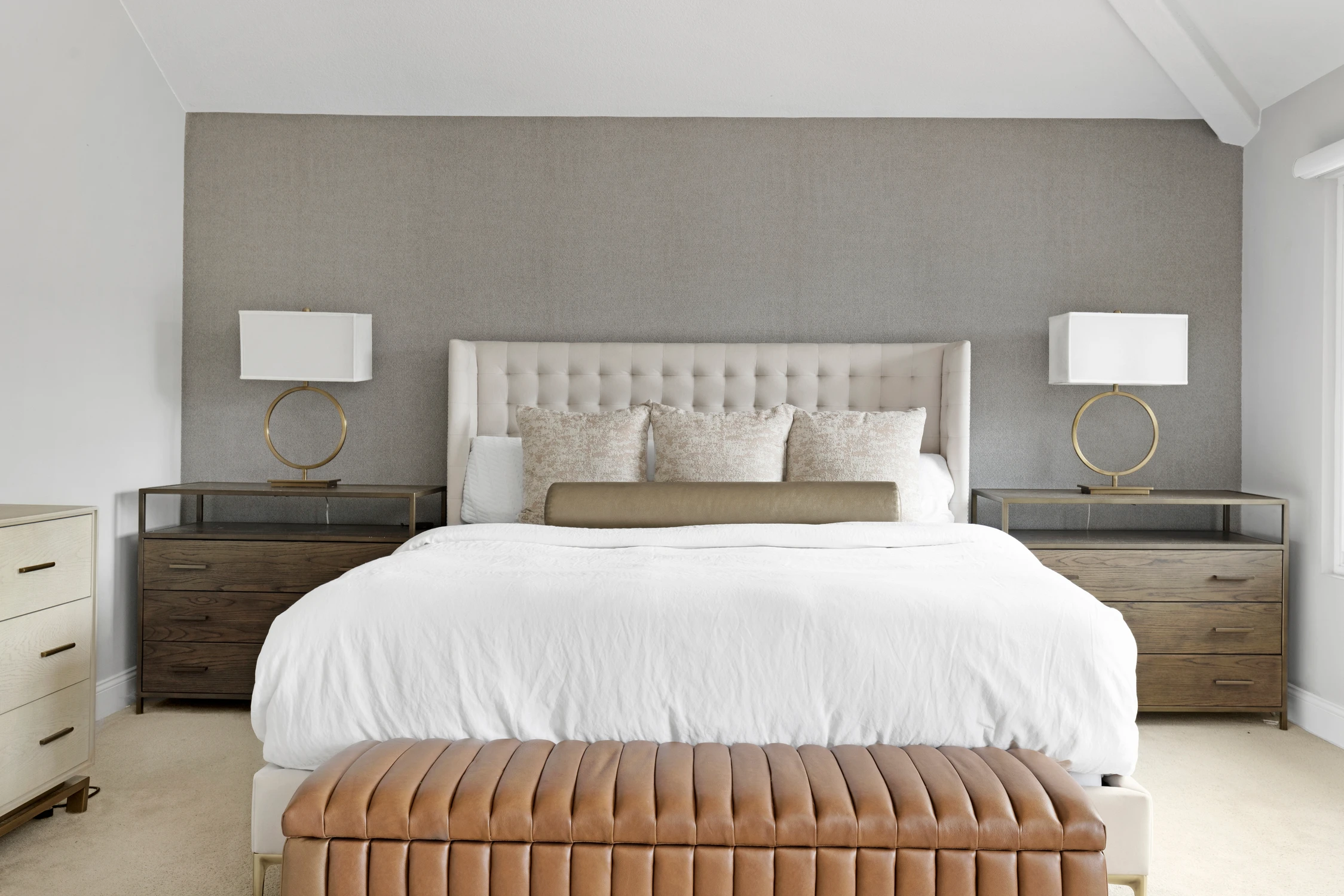 Bedroom with tufted white headboard, gray nightstands, and tan bench