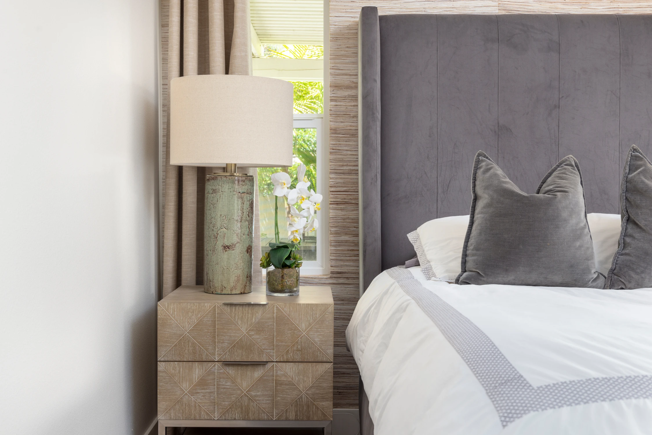 Bedroom nightstand beside dark gray bed and tall window