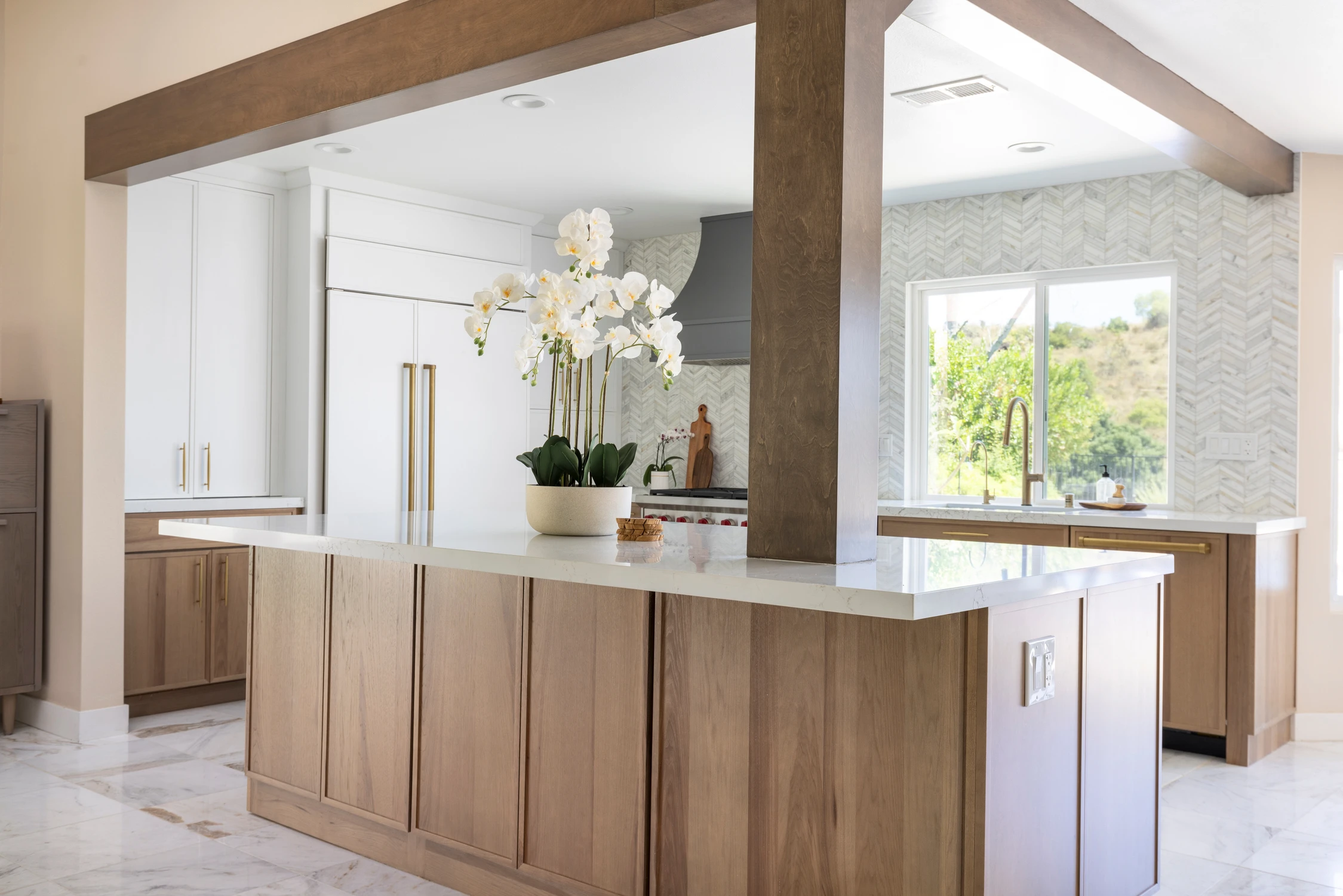 Kitchen island beneath exposed wood beams and an orchid centerpiece