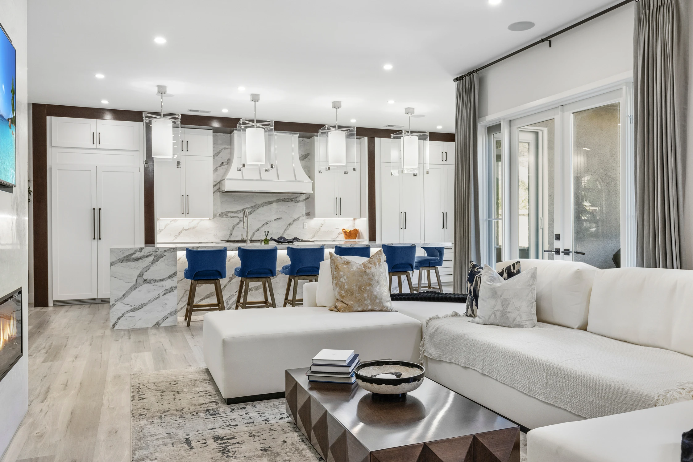 Open white kitchen with blue stools, marble island, and adjacent living room