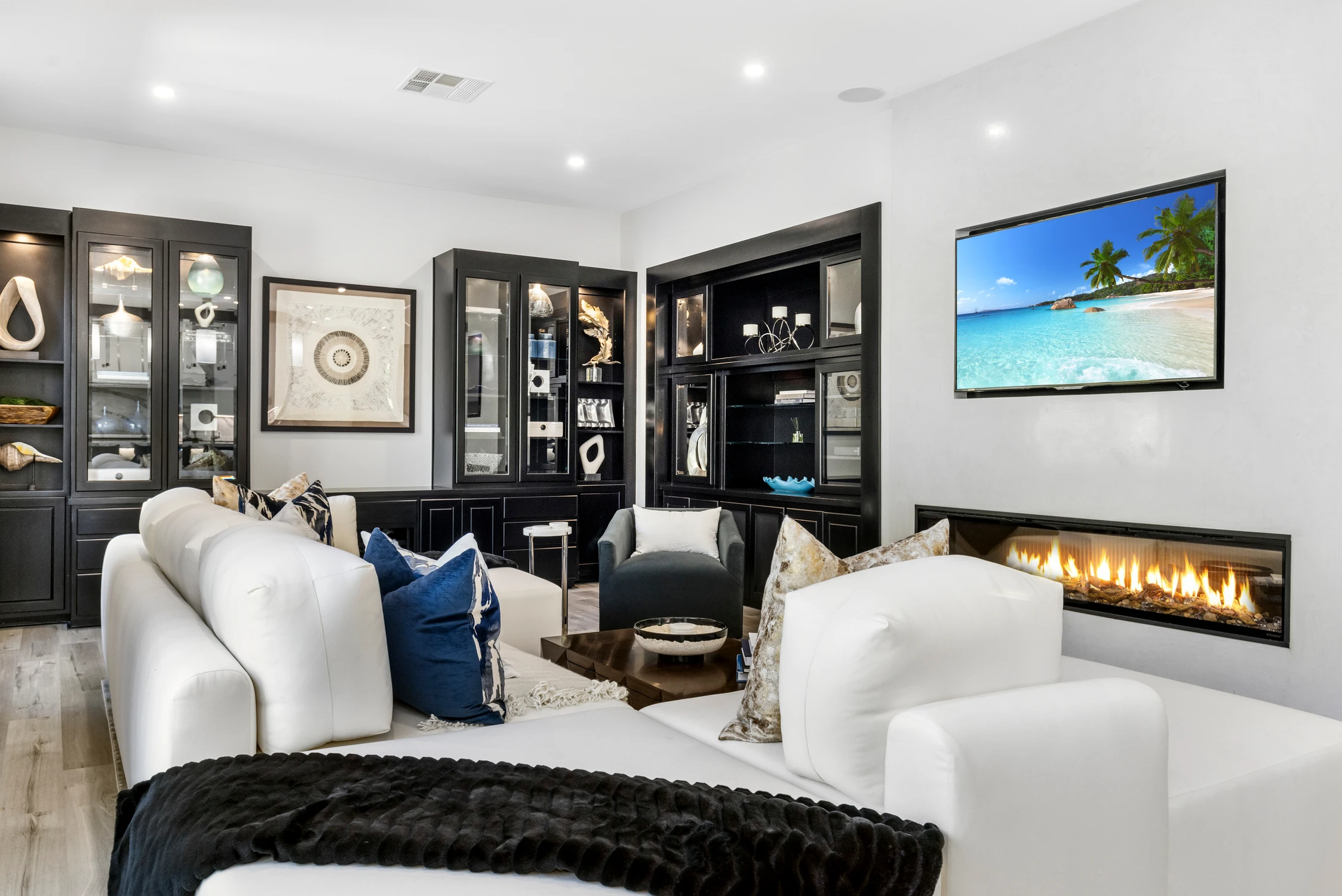 Family room with white seating, black built-ins, television, and linear fireplace