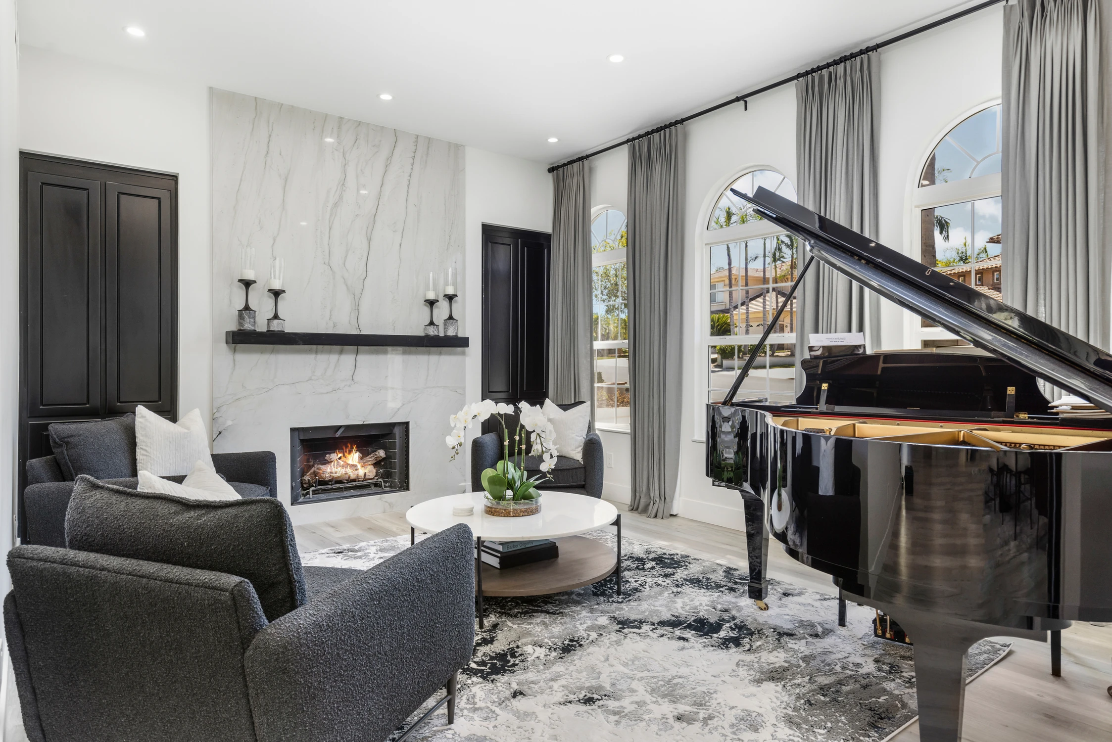 Music room with black grand piano, marble fireplace, and arched windows