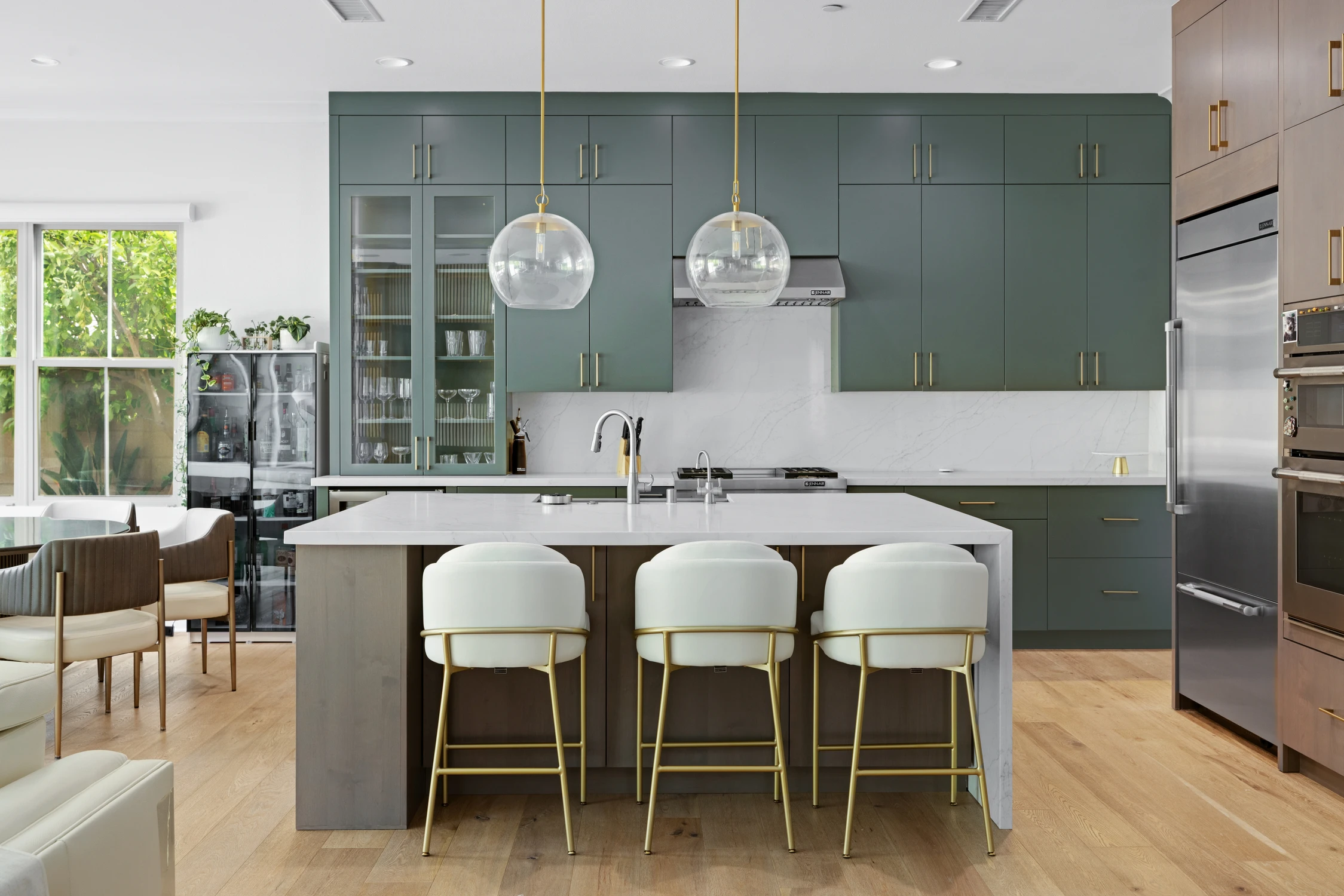 Kitchen island with green cabinetry, globe pendants, and upholstered counter stools