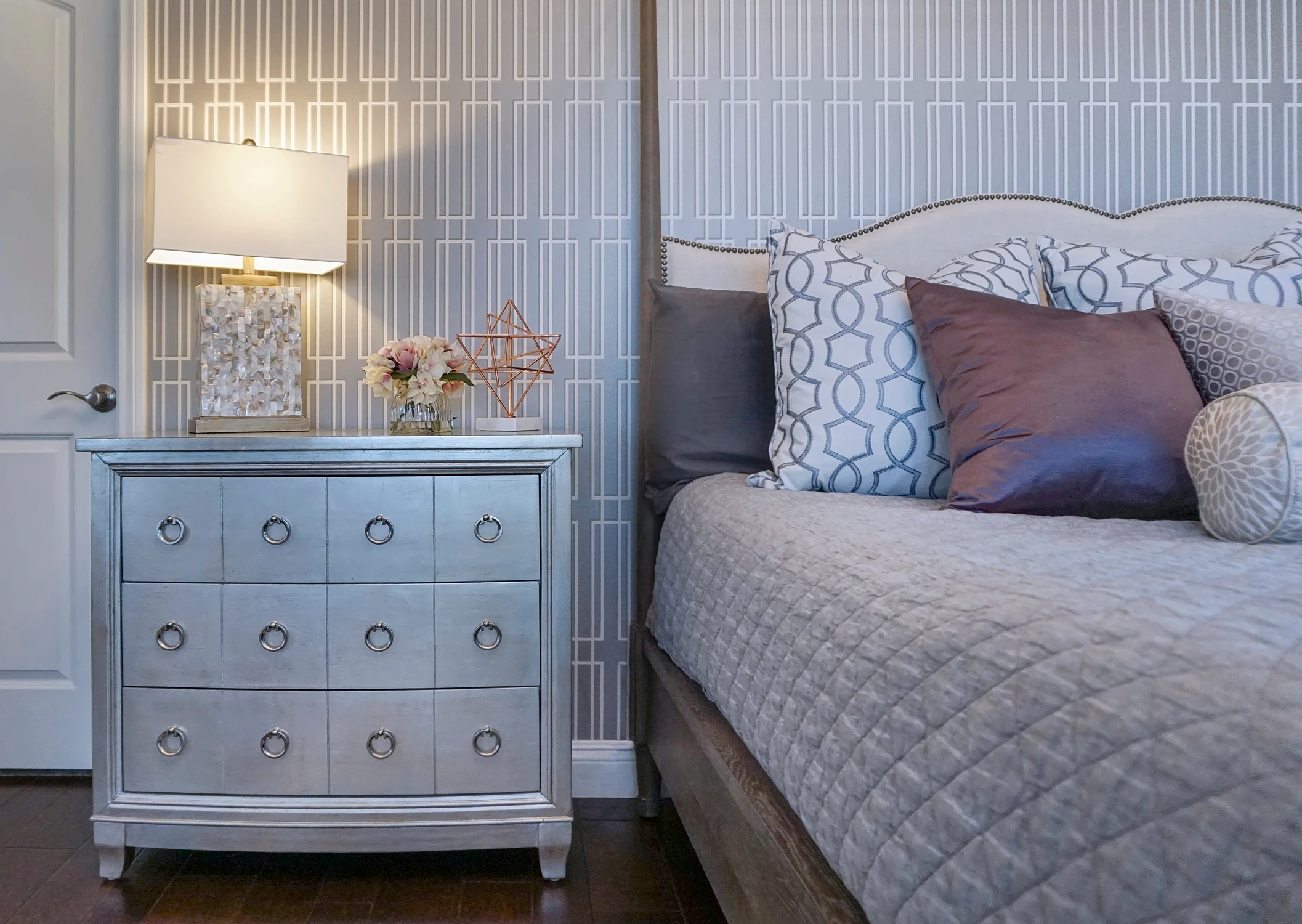 Bedroom nightstand beside patterned pillows and gray upholstered headboard
