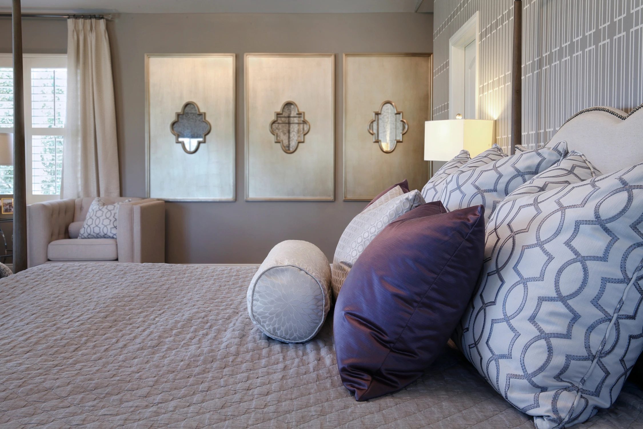 Master bedroom bedding with purple pillows and mirrored wall panels