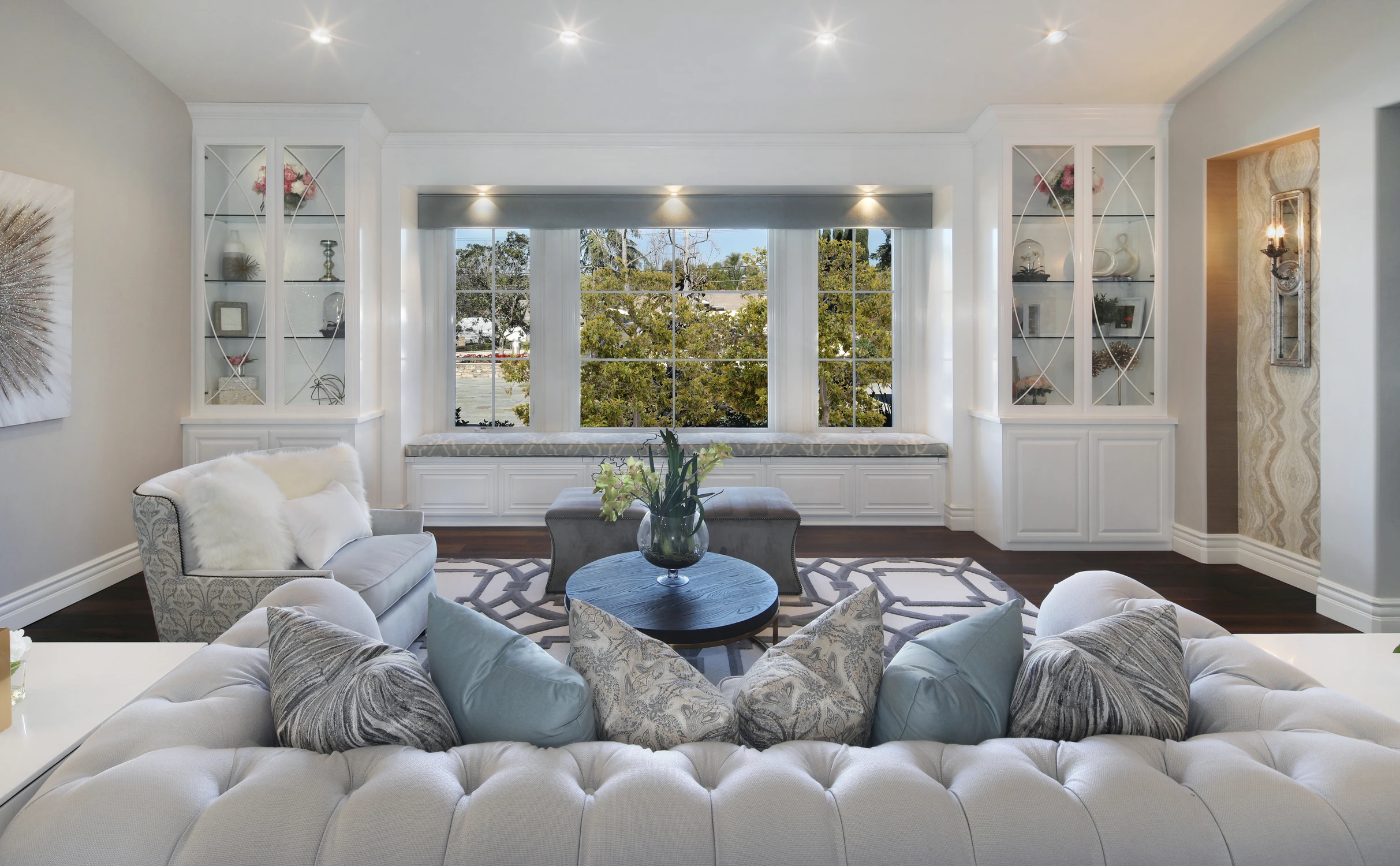 Formal living room with pale sofas, built-in shelves, and round blue ottoman