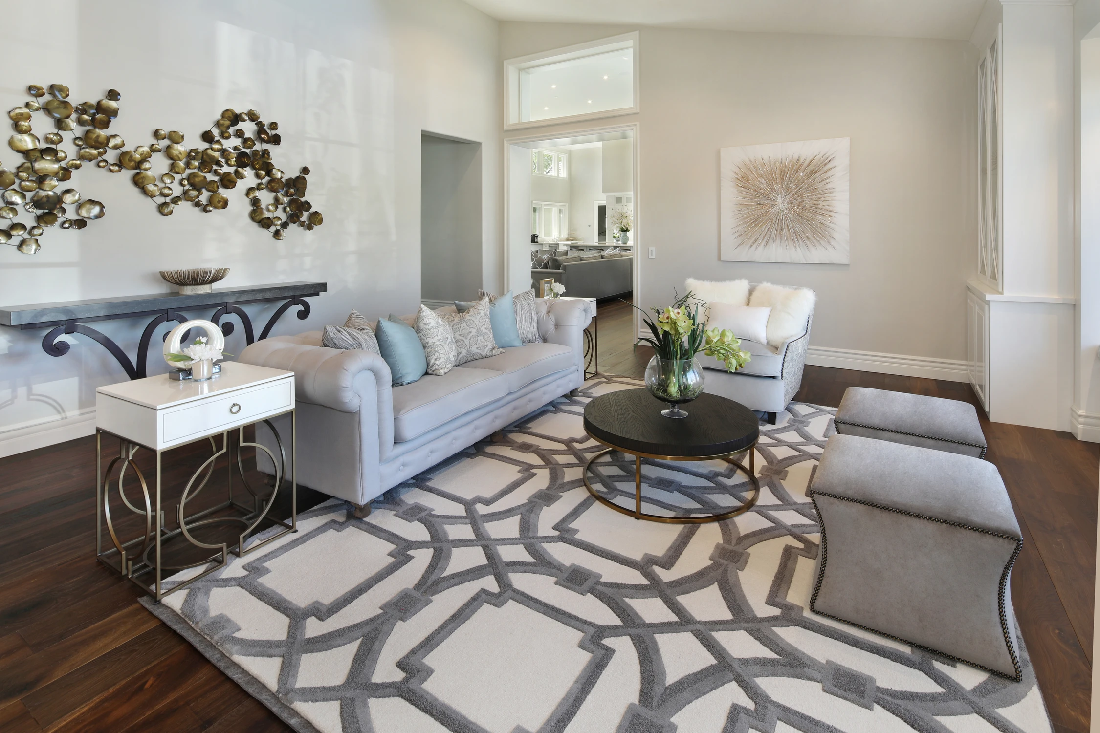 Formal living room with pale sofas, metal wall sculpture, and patterned rug